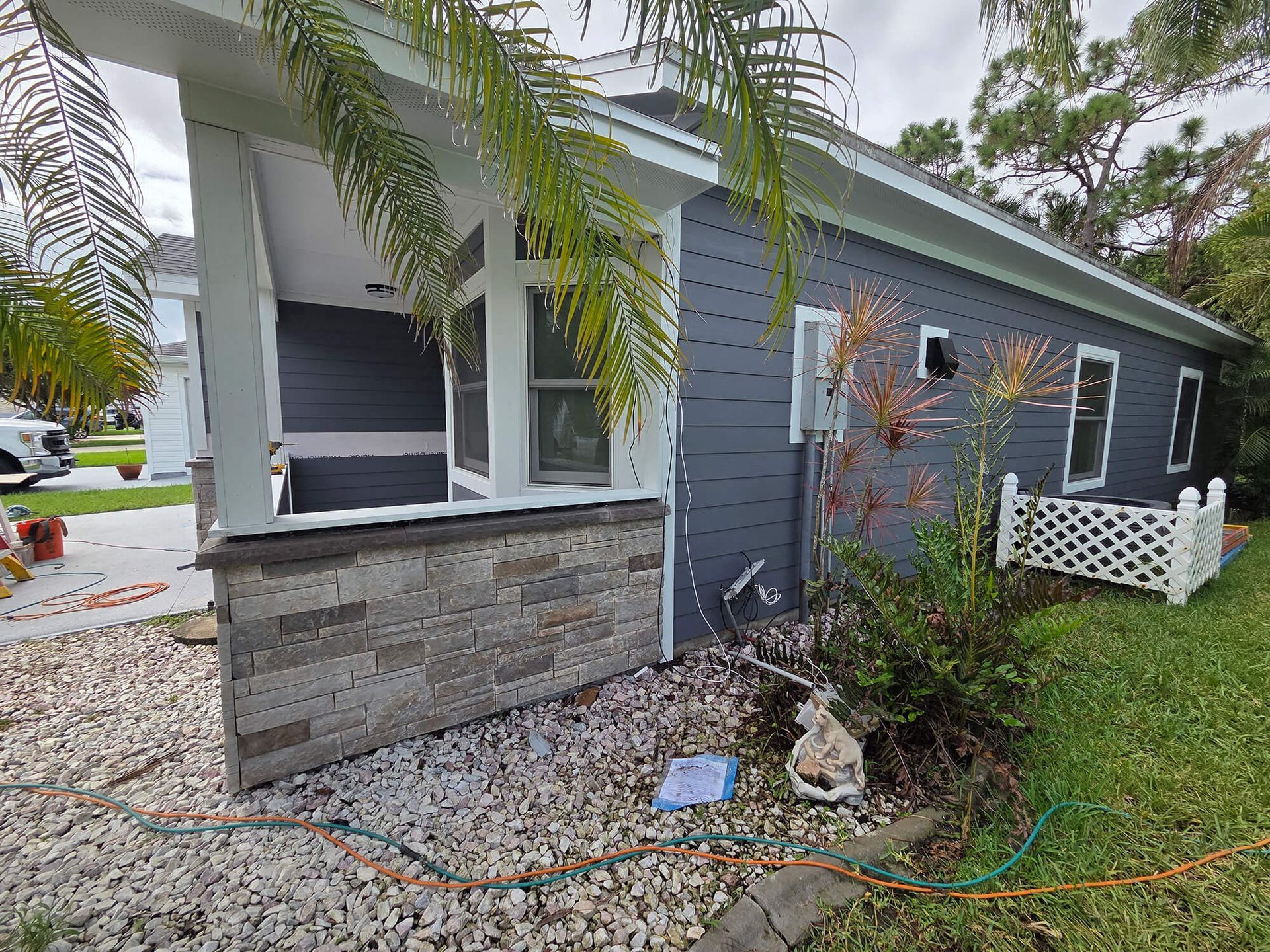 Small blue house exterior with stone lower wall, white porch railing, and front garden stones.