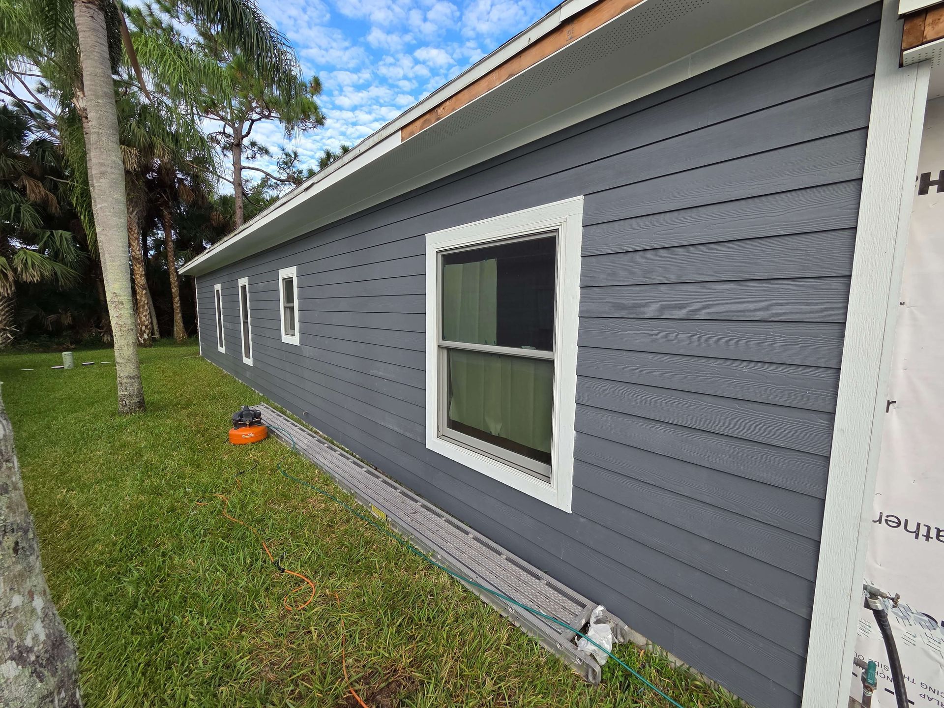 Gray house exterior with white-trimmed windows and a grassy yard beside it