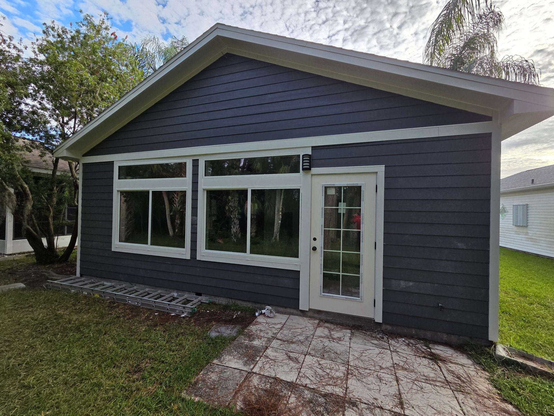 Small gray house exterior with white trim, large front windows, and a white front door by a patio.