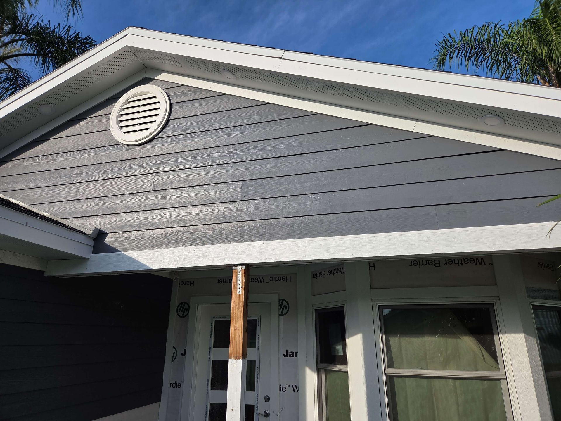 Gray house exterior with white trim, front porch, and circular attic vent under a blue sky