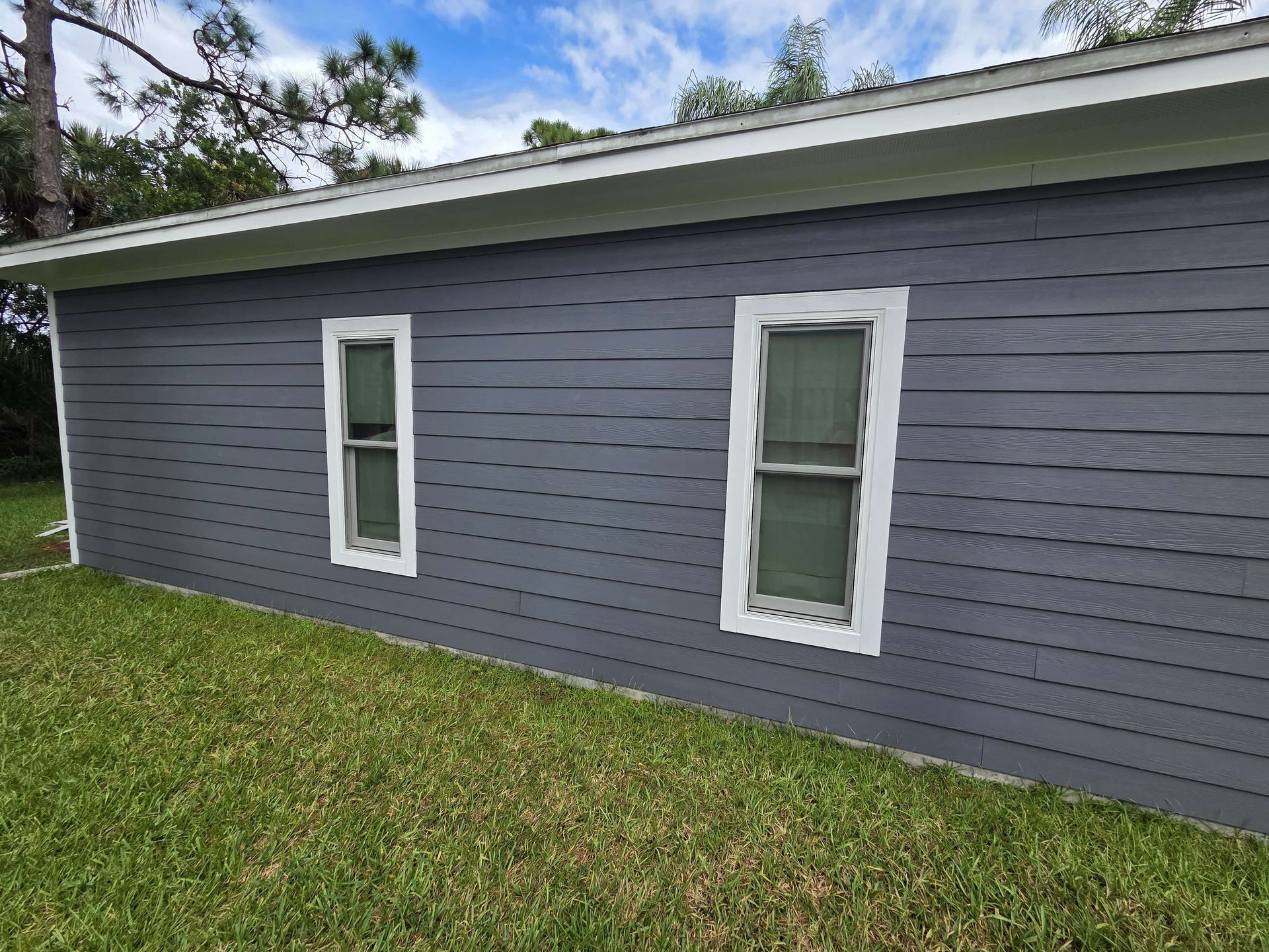Side of a gray house with two white-trimmed windows and a green lawn.