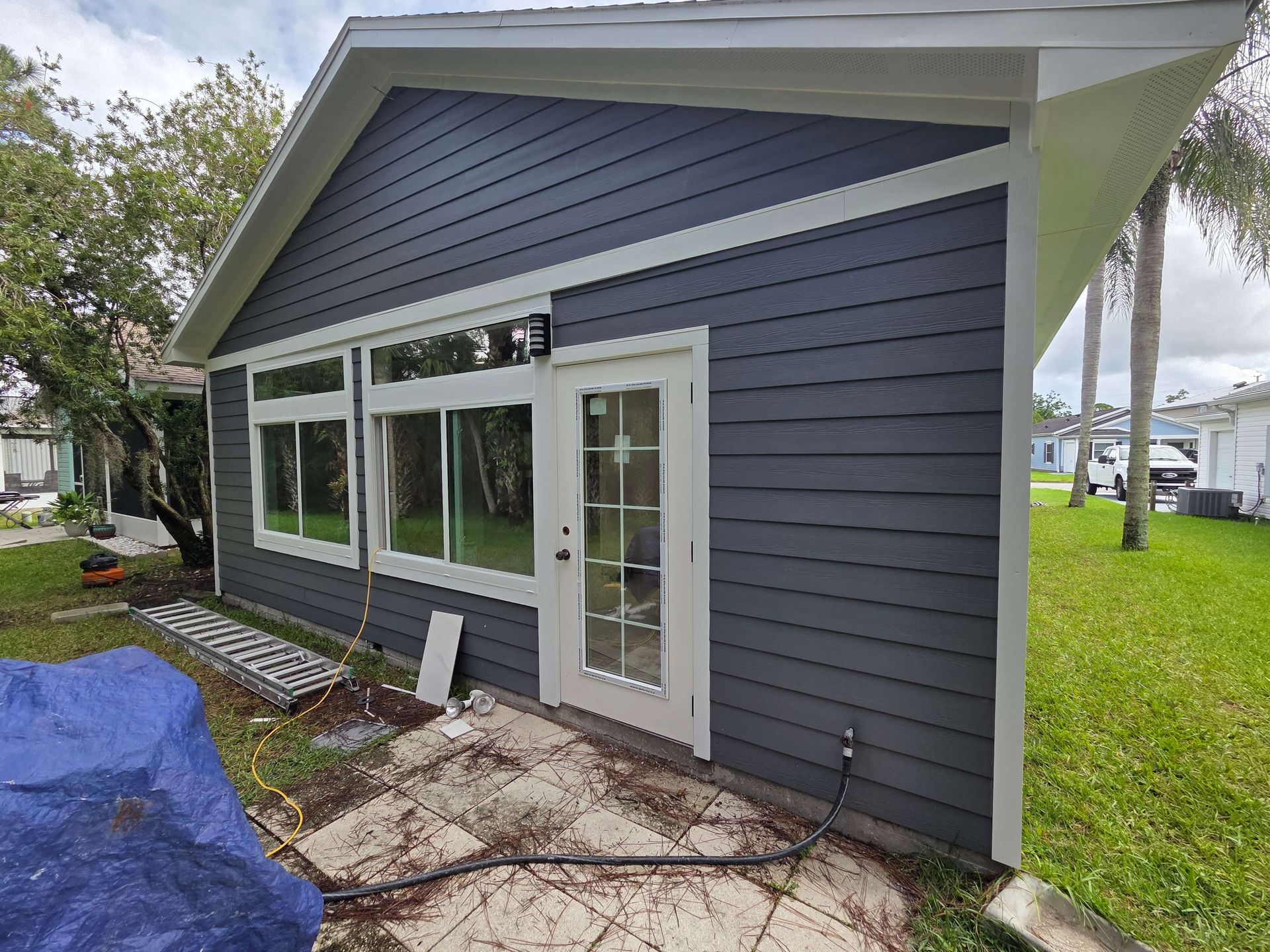 Gray modern house exterior with white-trimmed windows and a glass door, viewed from the side.