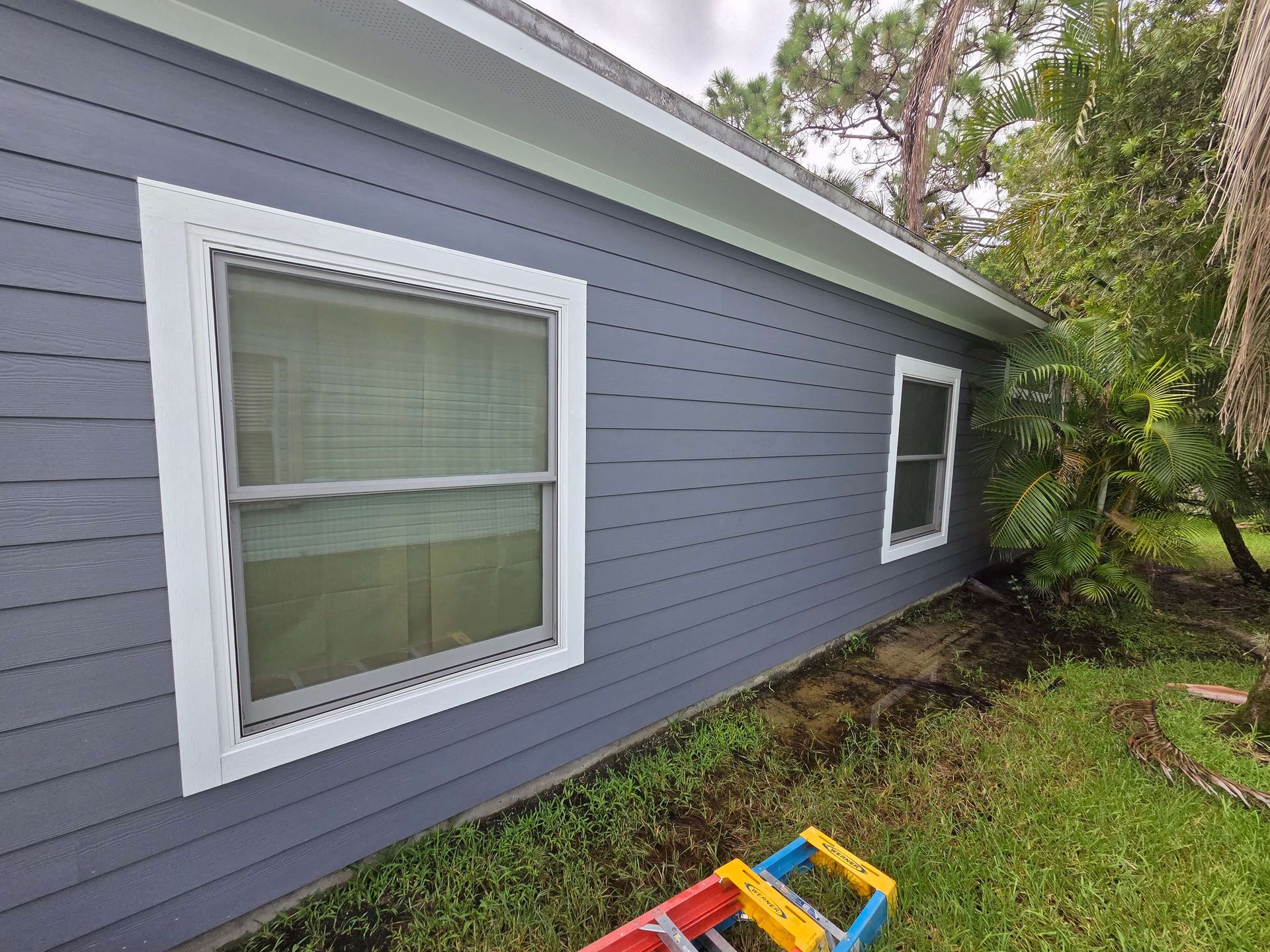 Gray house exterior with white-trimmed windows and a colorful toy on the grass beside the wall