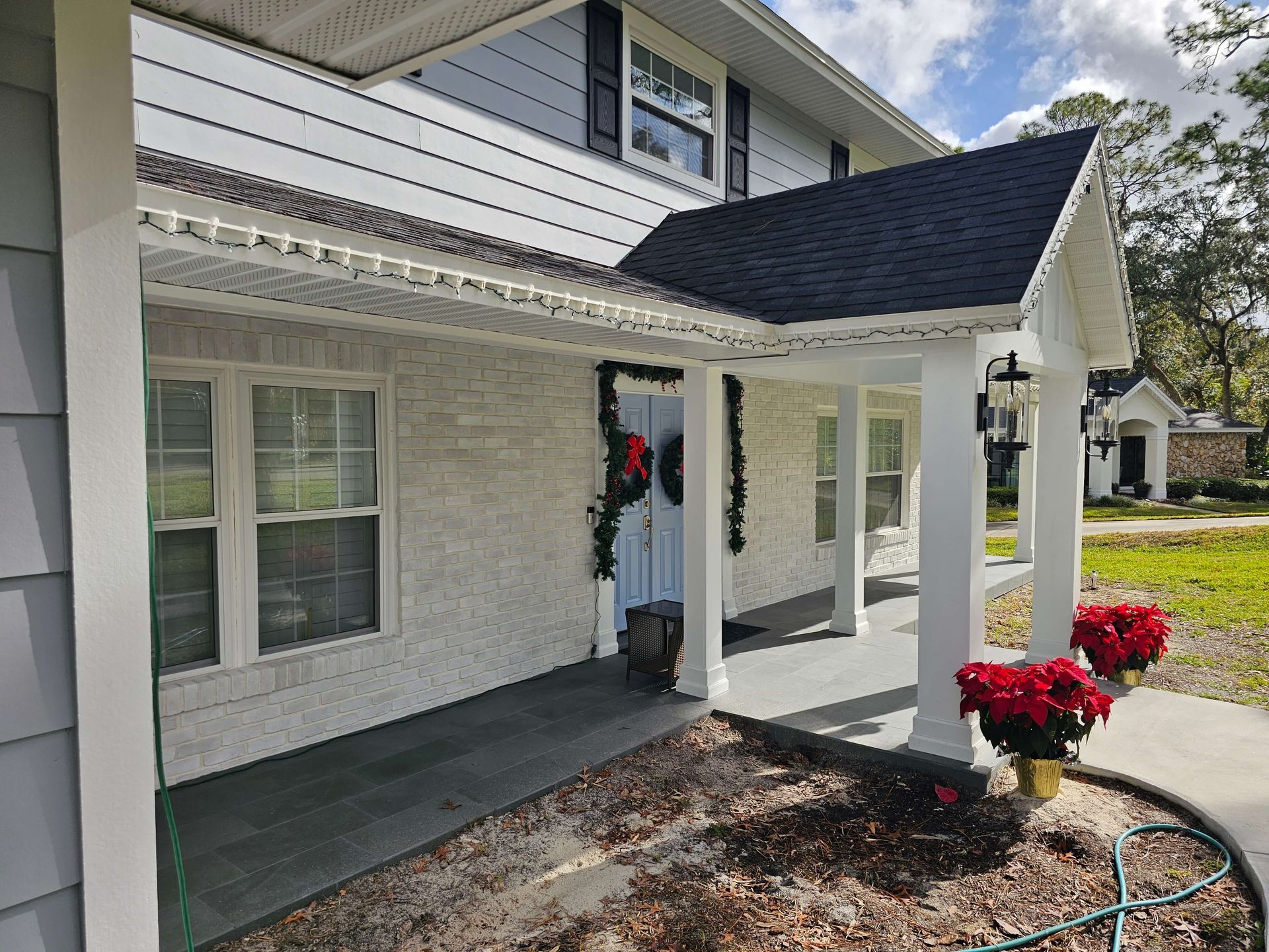 White house porch with covered entry, black roof, and red potted flowers along the walkway