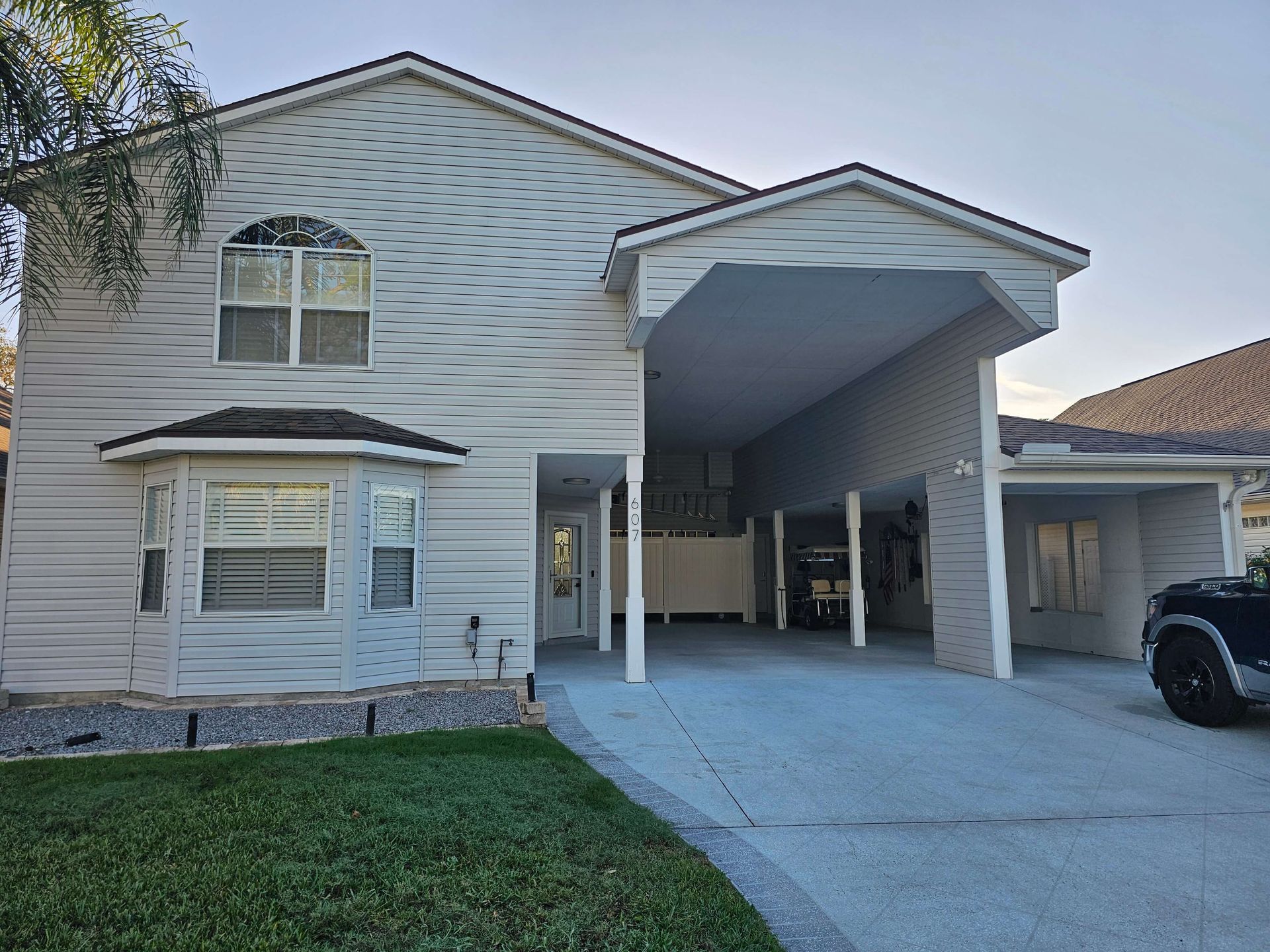 Two-story suburban house with a covered driveway and carport, white siding, and a car parked on the right.