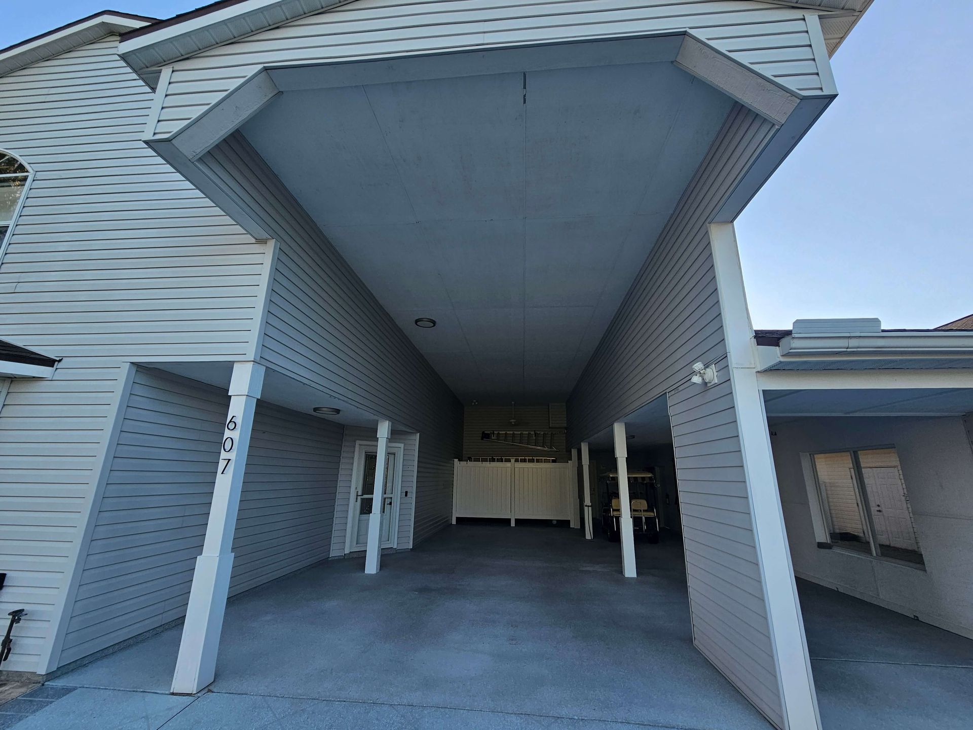 Covered apartment breezeway with white siding and garage doors on both sides.