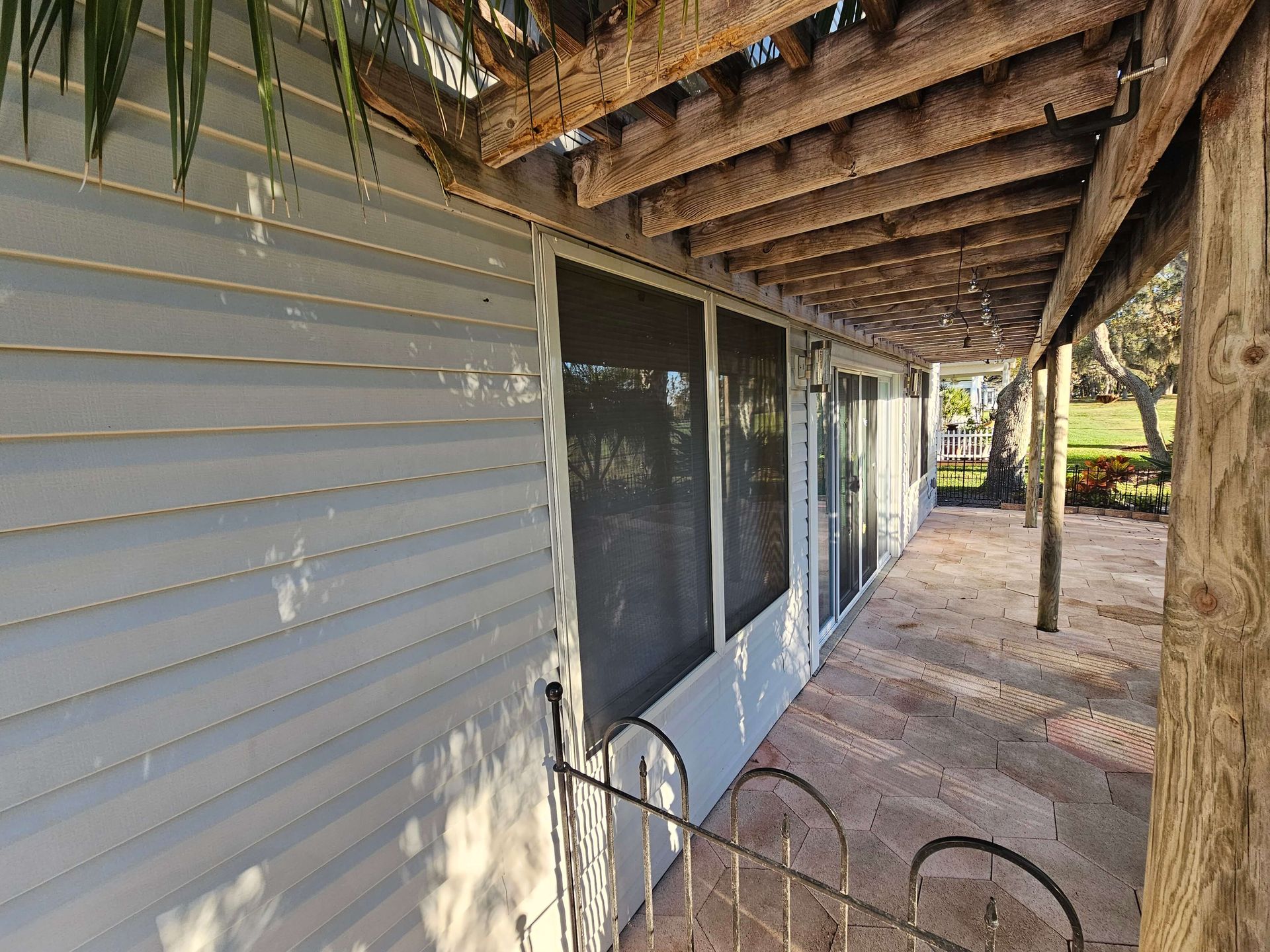 Covered porch beside a white house with sliding glass doors, wooden beams, and a brick walkway