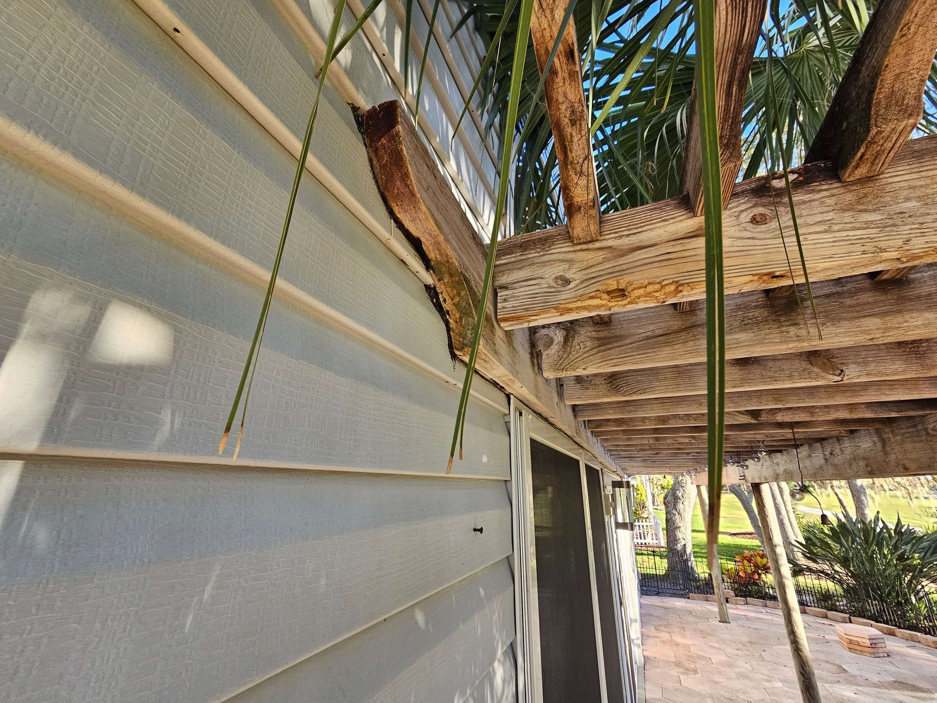 Close-up of a weathered wooden palm structure beside a white corrugated wall outdoors