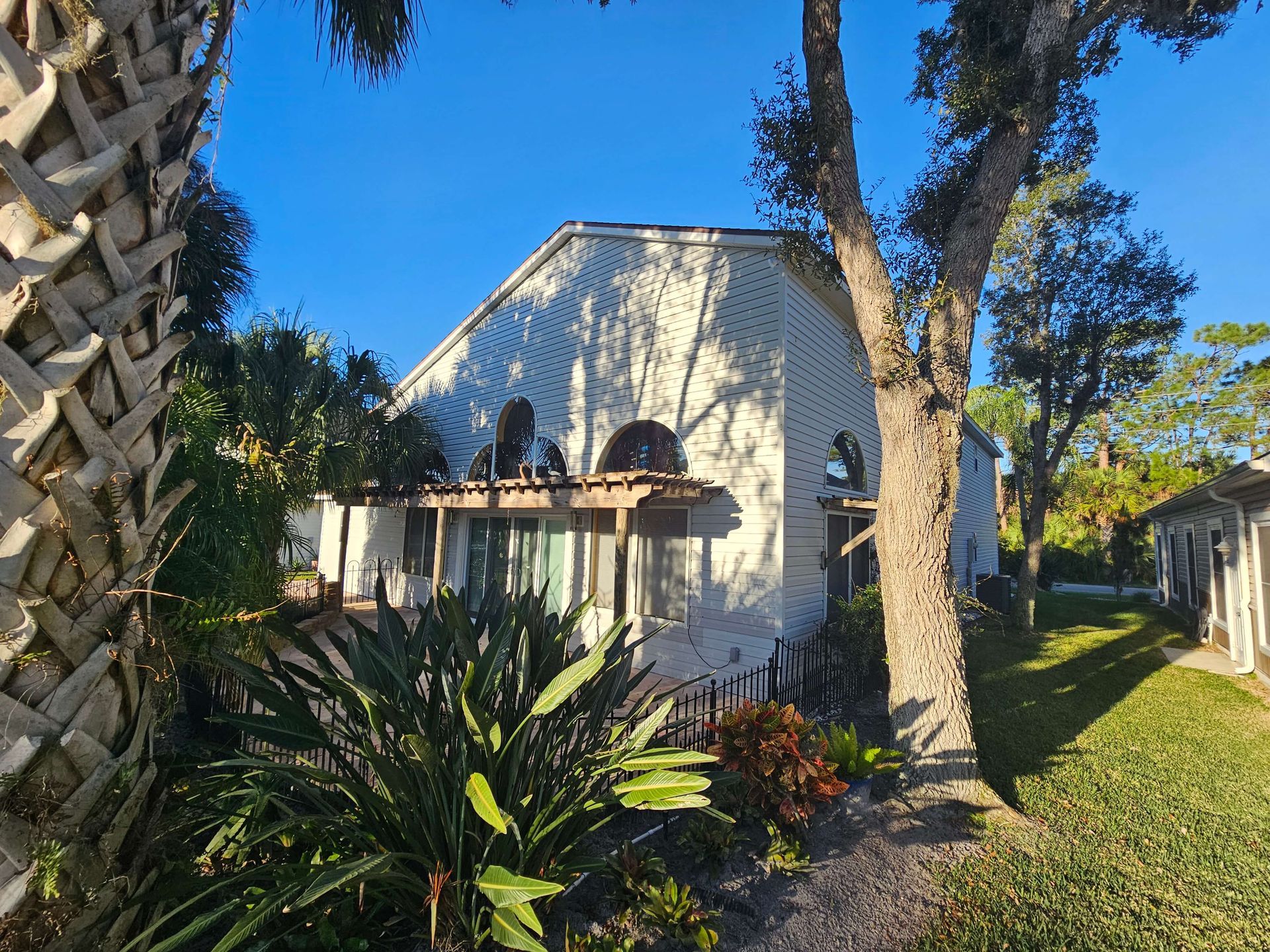 White stucco house with arched windows, palm trees, and lush garden in bright sunlight