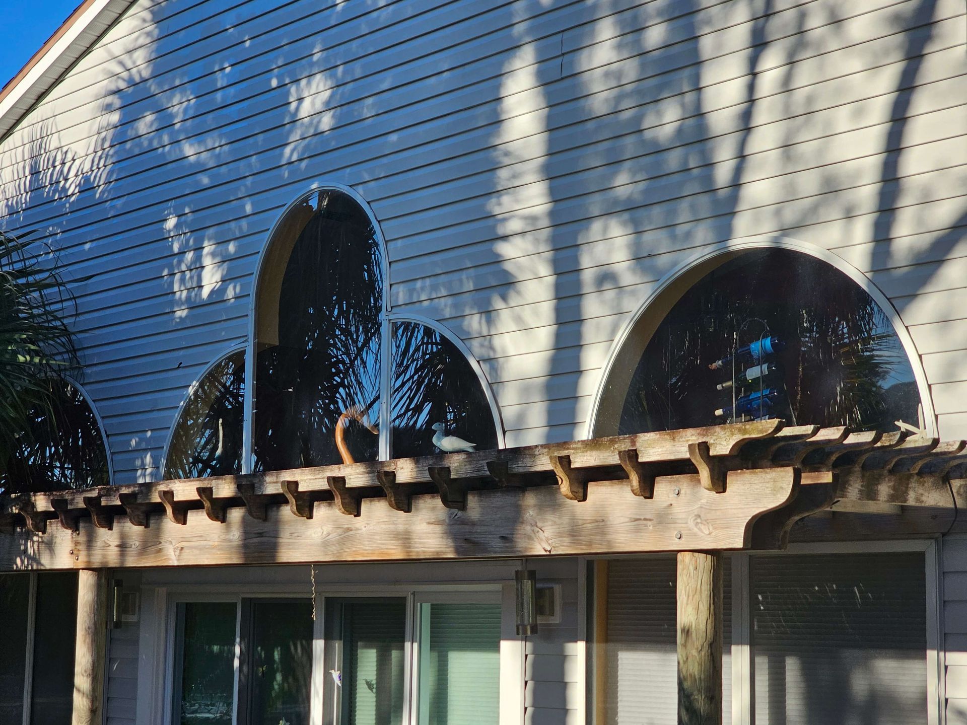 Building facade with arched windows, wooden pergola, and leaf shadows in sunlight