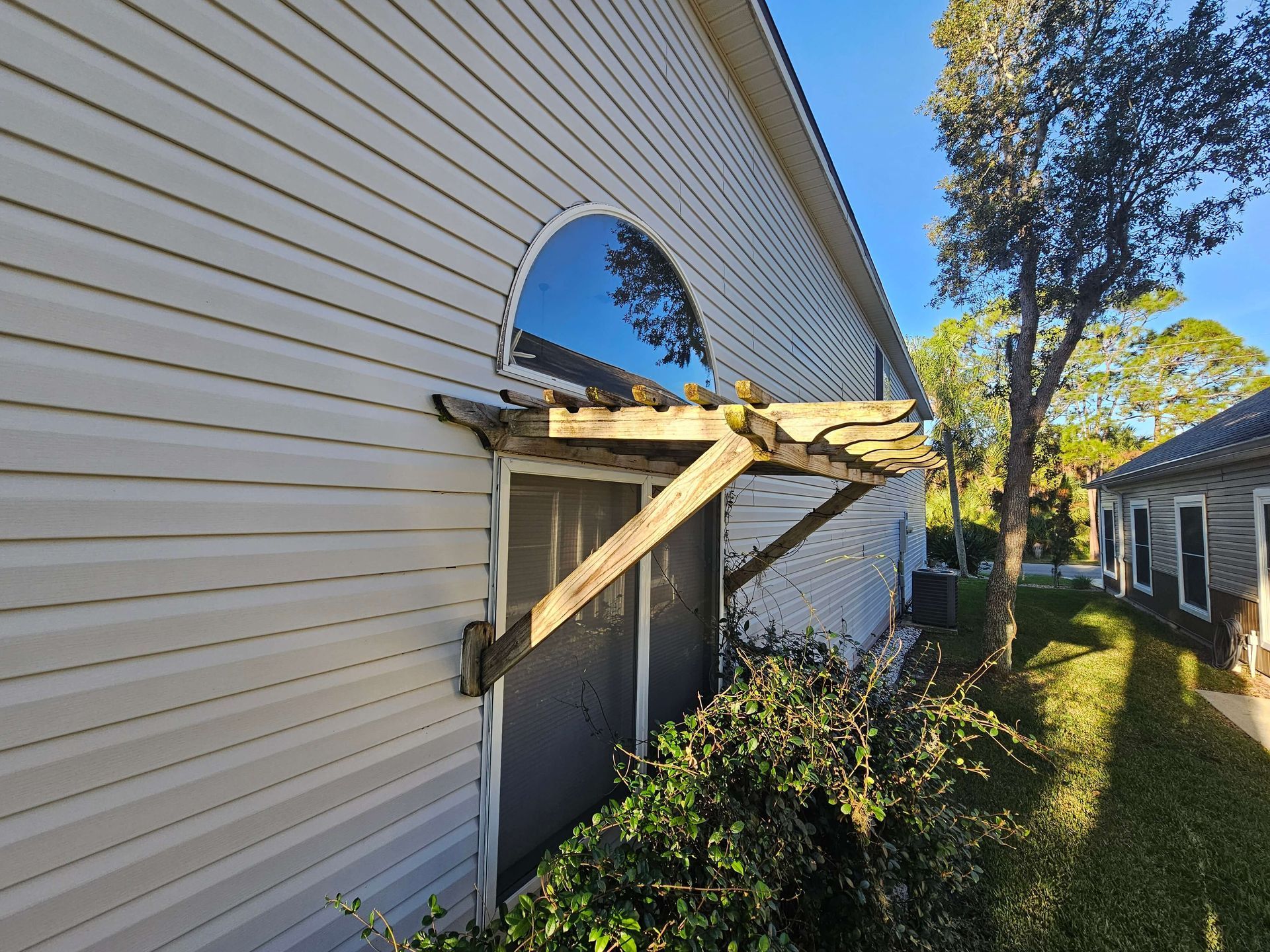 Damaged exterior wall with a broken arched opening and makeshift wooden supports beside a house
