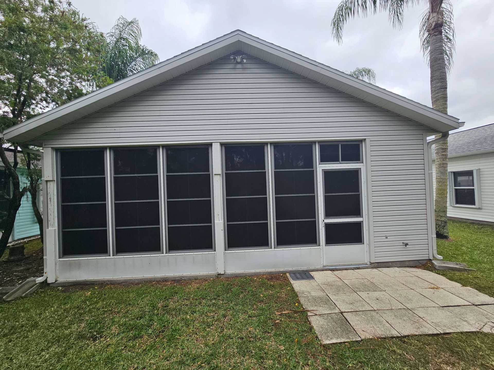 Front view of a gray house with screened windows and a small concrete patio.