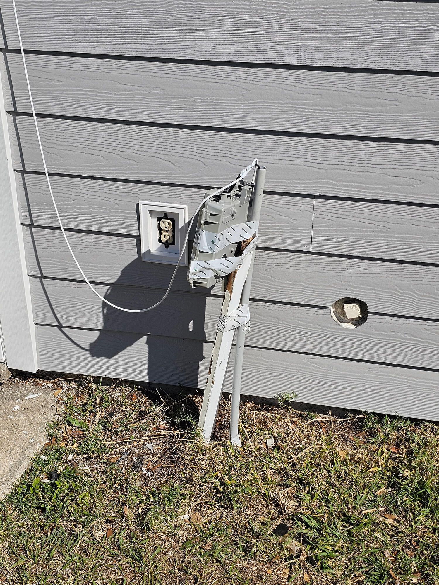 Damaged outdoor utility meter box and cable on gray house siding near the ground