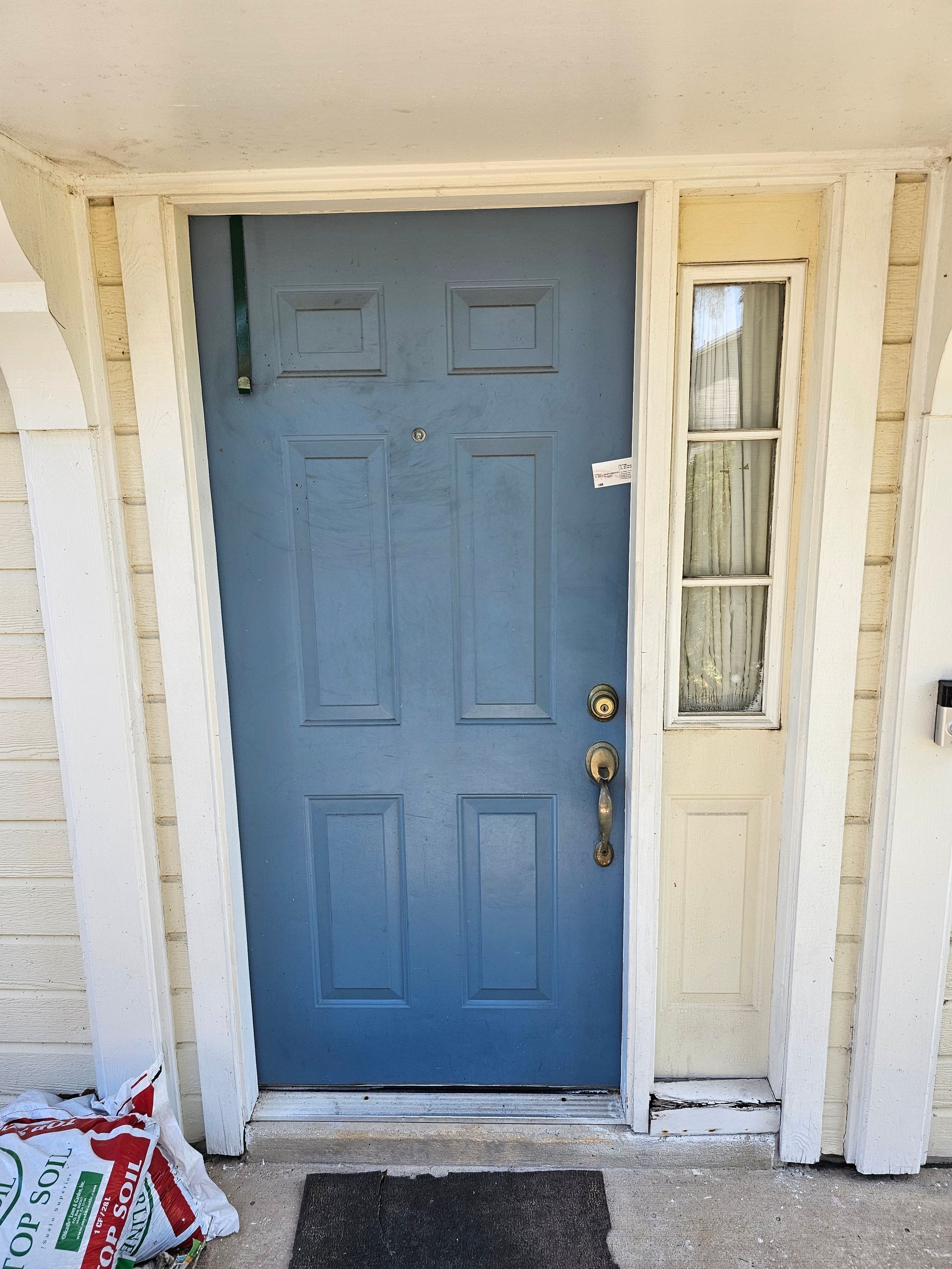 Blue front door with a narrow glass side panel and white trim, viewed from the porch