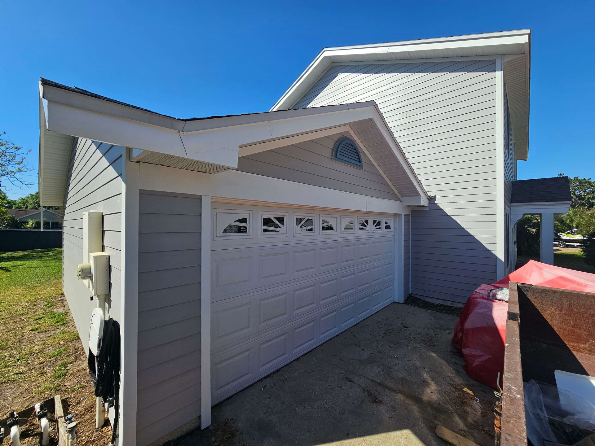 White garage beside a house with gray siding, seen from an angled driveway on a sunny day
