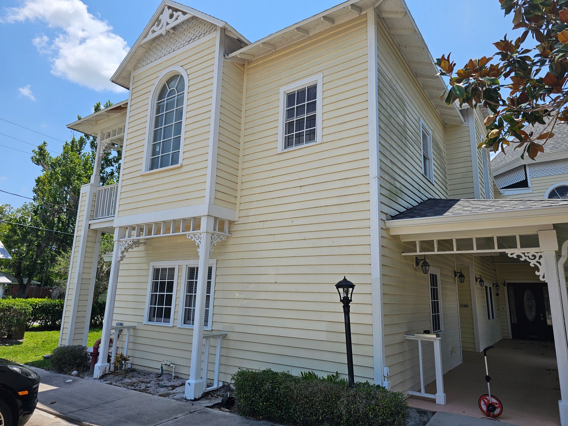 Two-story pale yellow house with white trim, arched windows, and a covered front porch under a blue sky