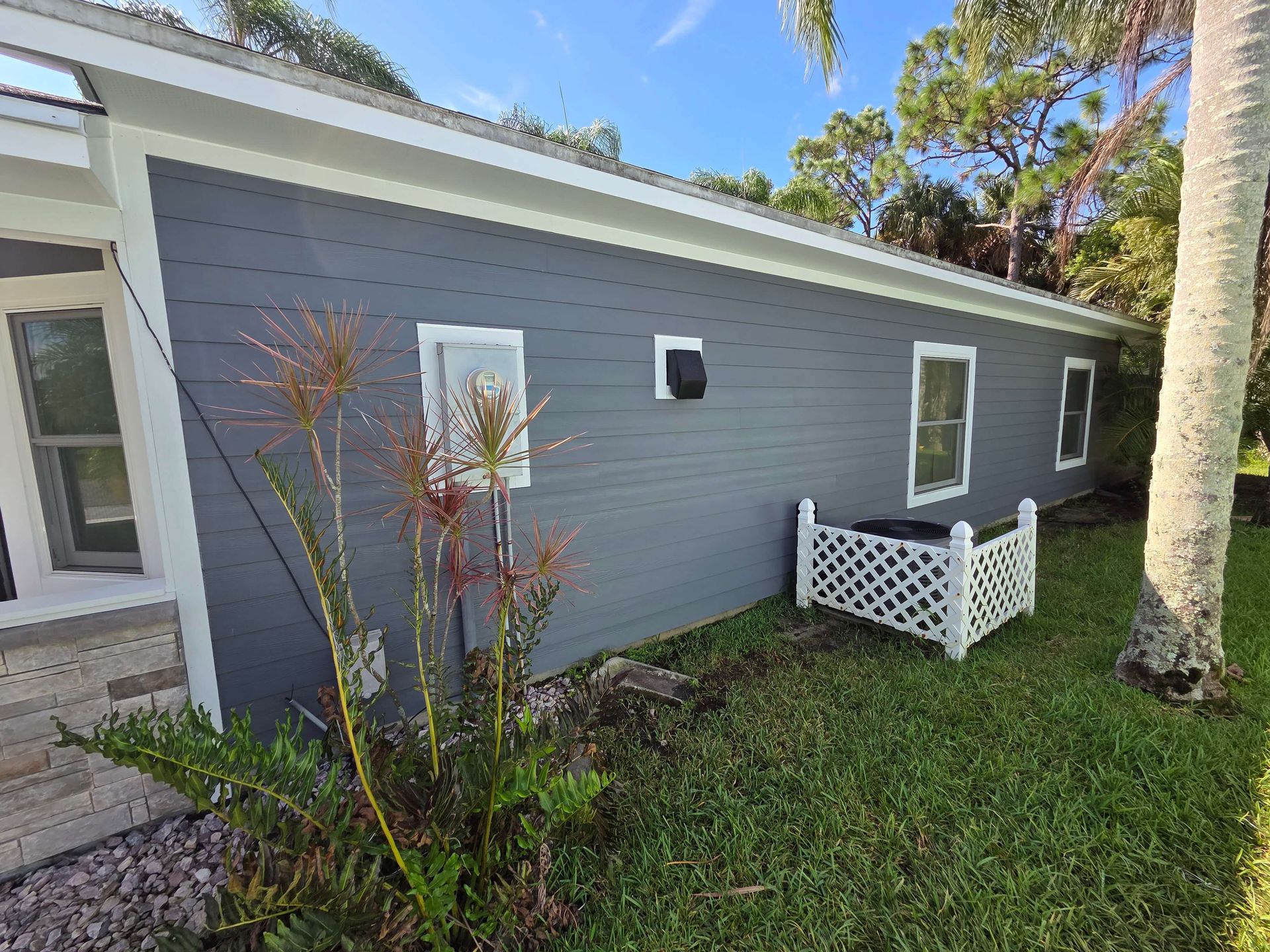 Gray house exterior with white trim, small windows, and a white bench in a grassy yard.