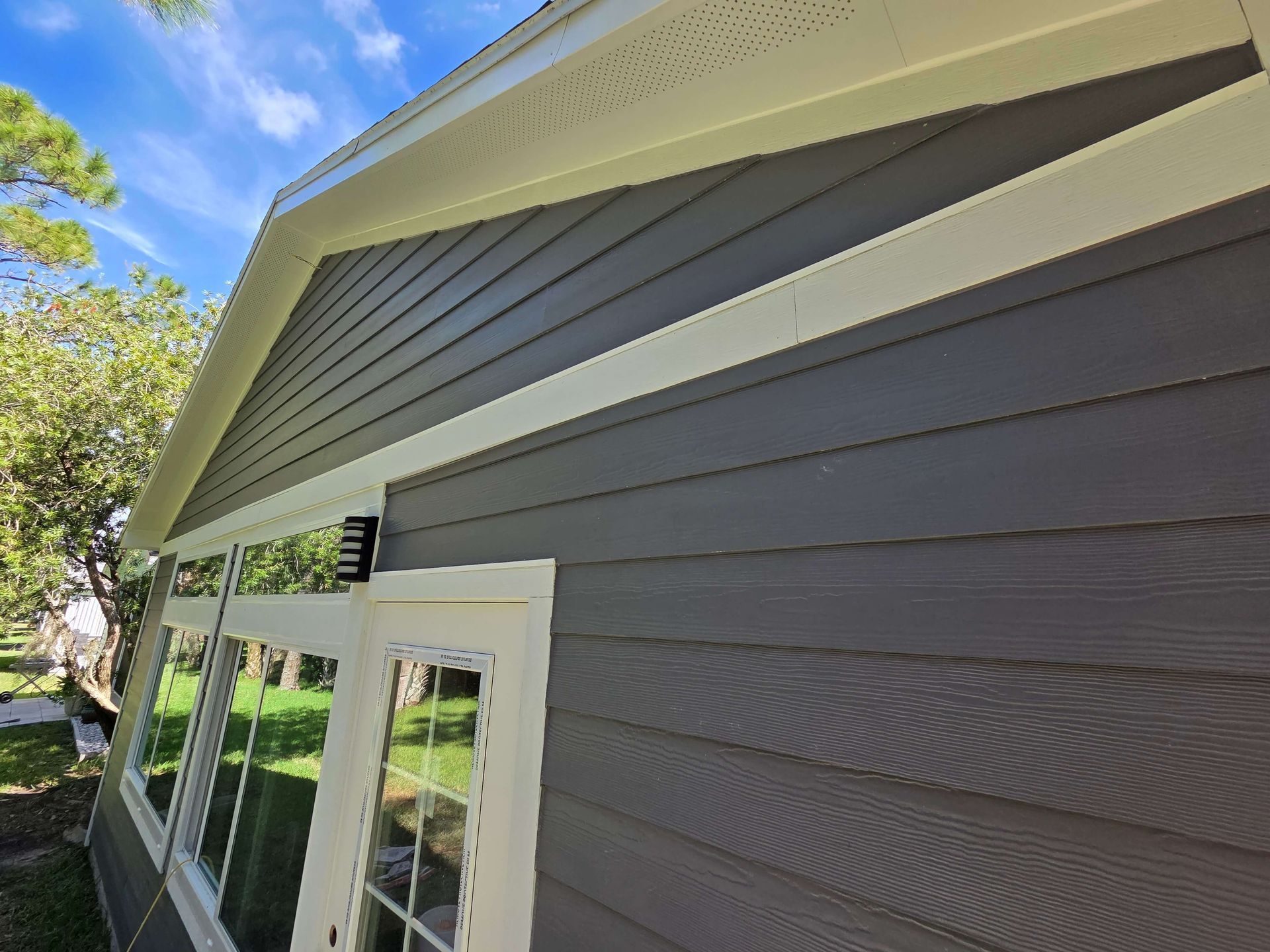 Close-up of gray house siding, white trim, and windows beneath a gabled roofline.