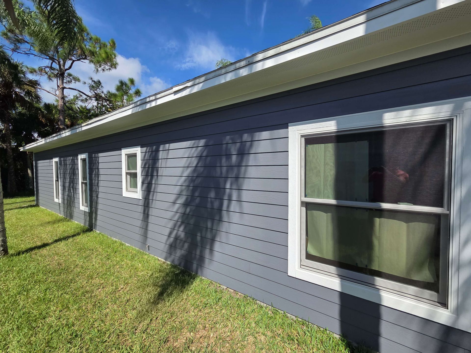 Gray house exterior with white-trimmed windows and a sloped roof beside a grassy yard