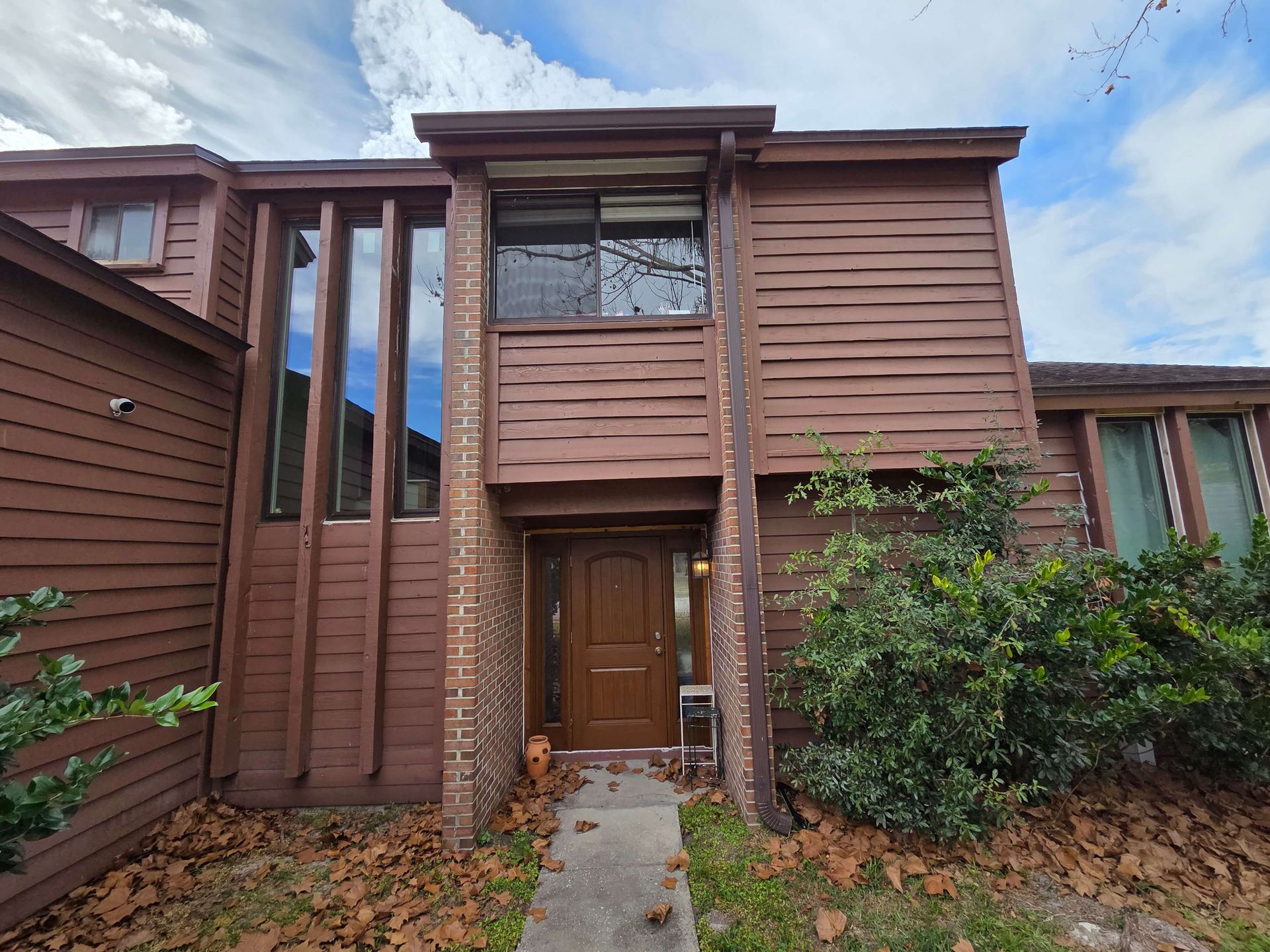 Modern brown townhouse exterior with a central front door and tall windows under a cloudy sky