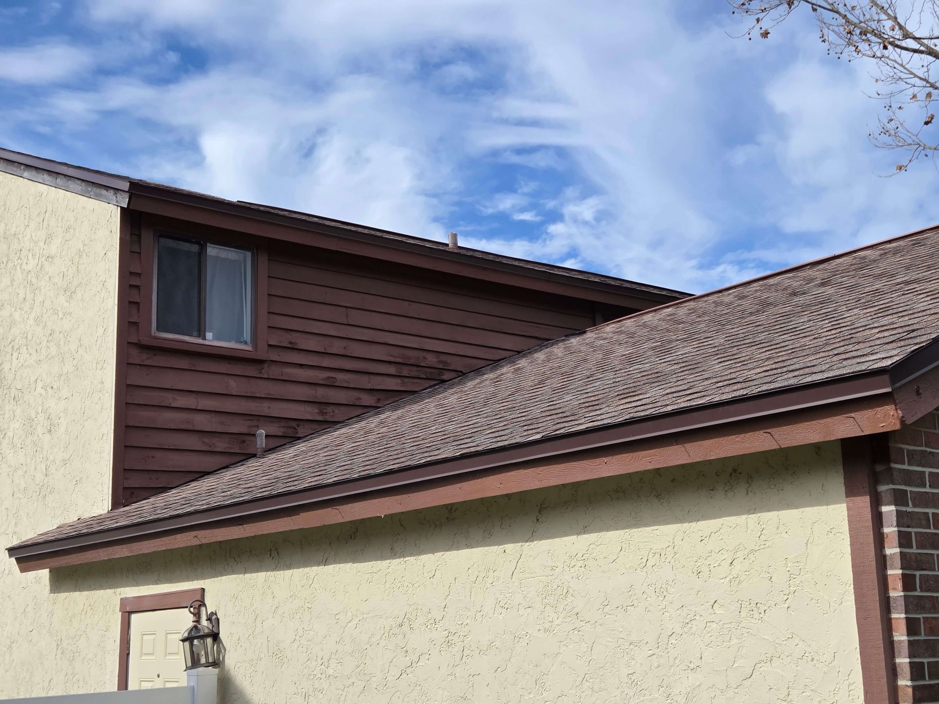 Suburban house roof and eaves under a partly cloudy blue sky
