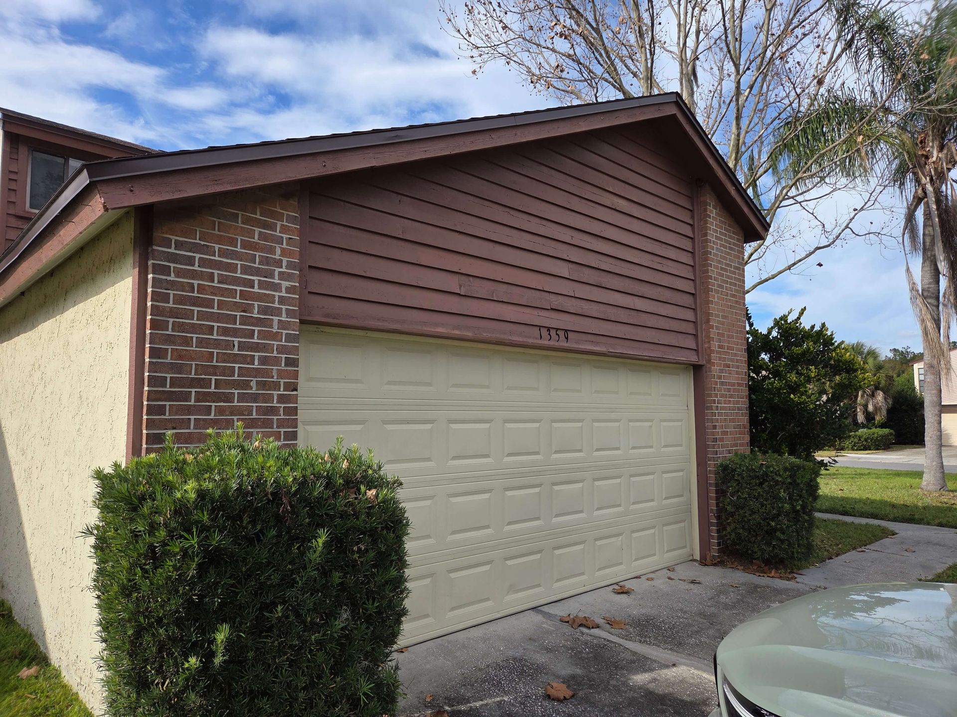 Suburban house garage with beige door, brick trim, and trimmed bushes in front