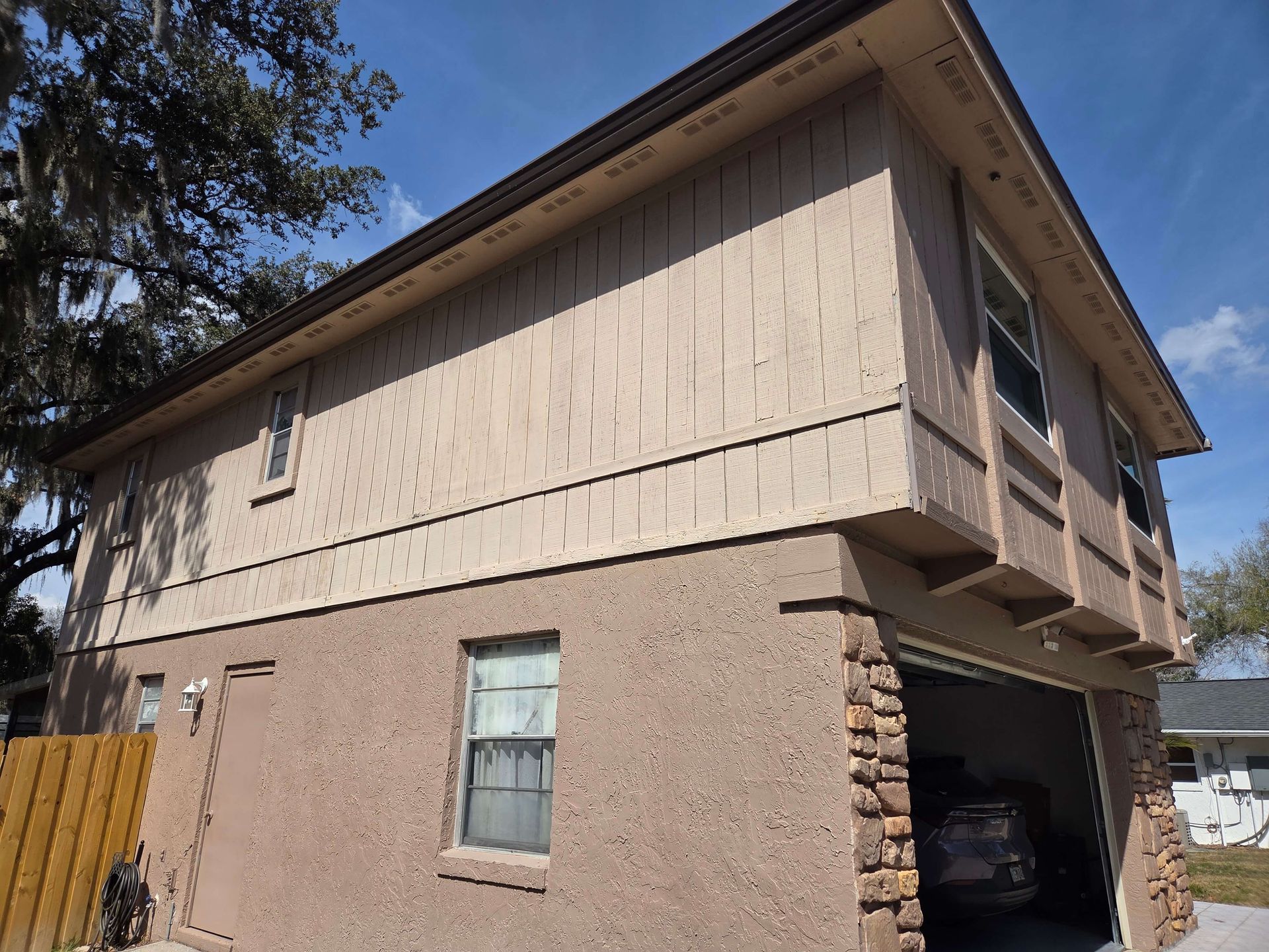 Two-story tan house with stone lower level and a carport under a sloped roof