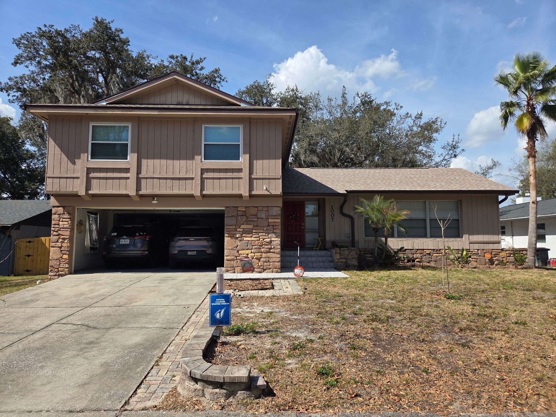 Suburban two-story house with stone accents, open garage, and dry front yard under a blue sky.