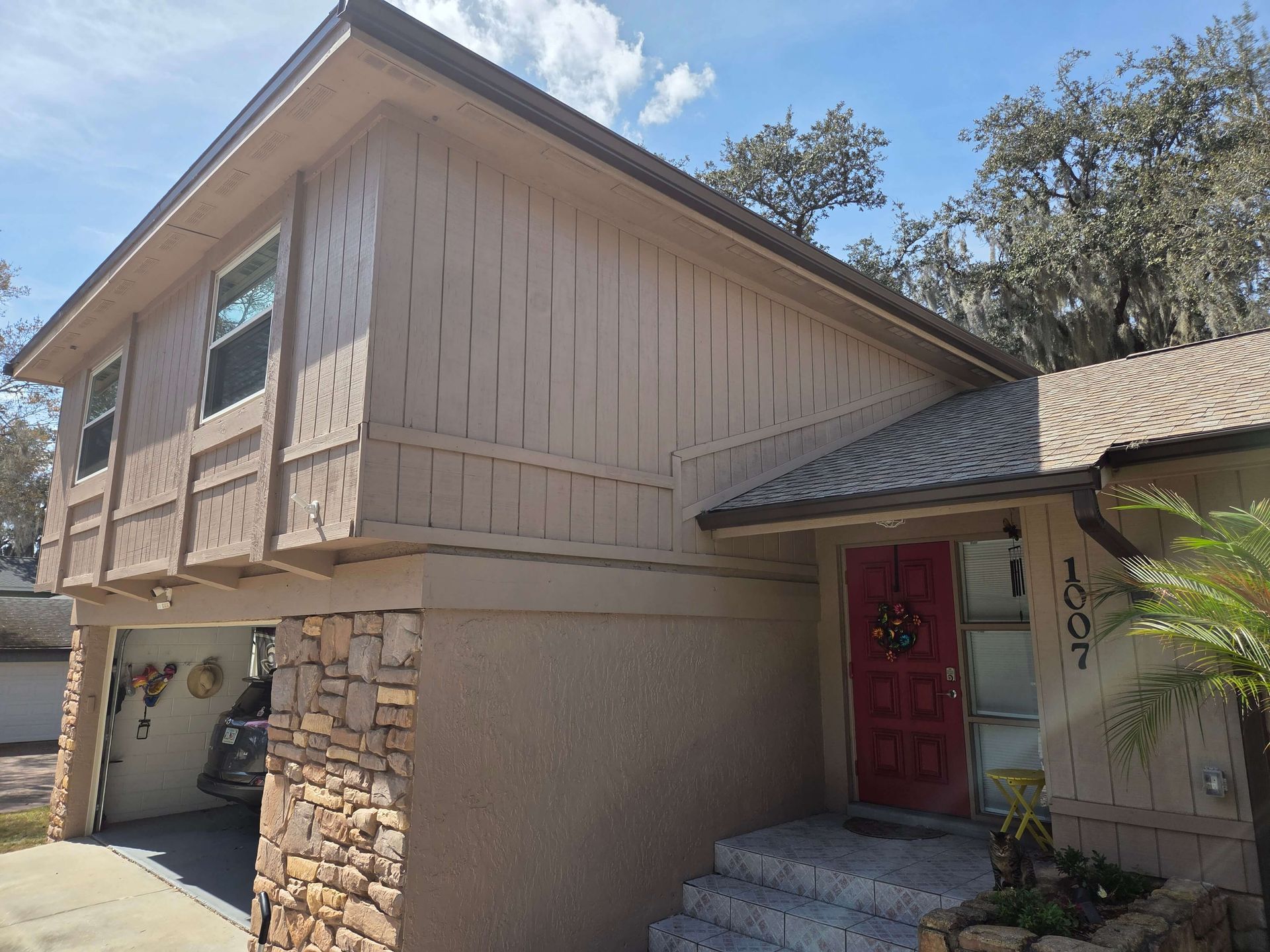 Two-story tan house with stone accents and a red front door under a tiled roof, viewed from the driveway