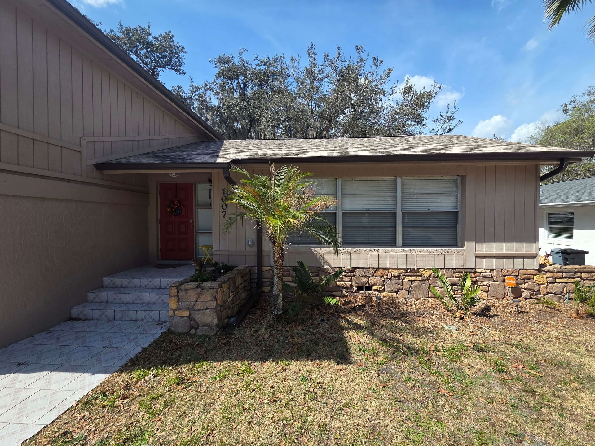 Single-story house exterior with red door, front steps, and a small palm tree by the entry.