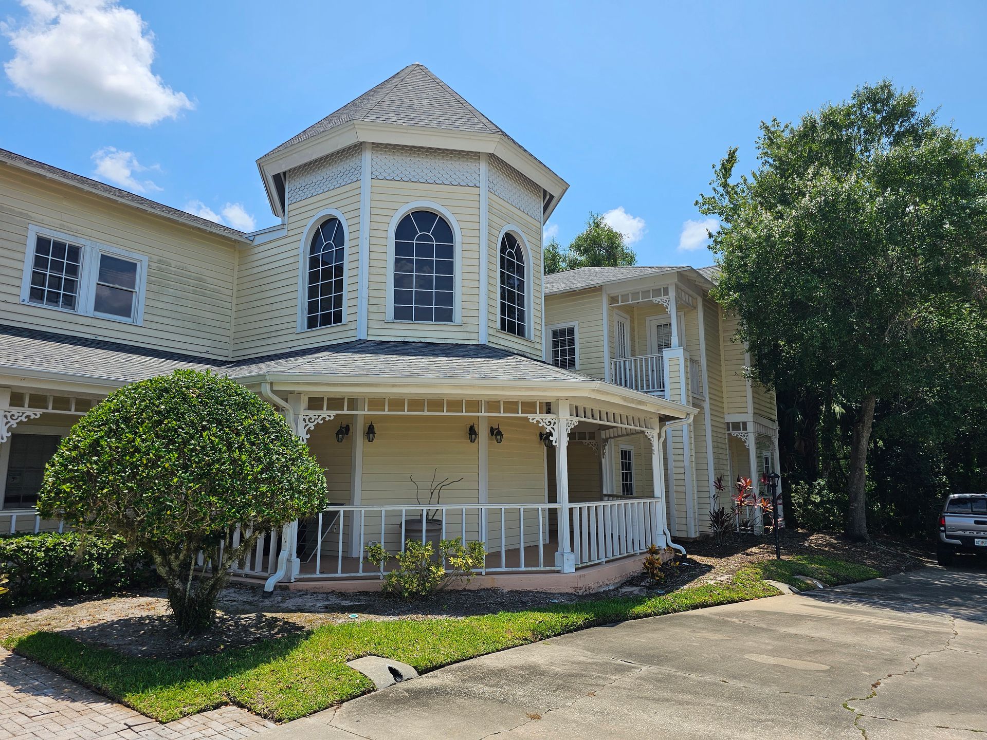 Two-story cream house with a wraparound porch, turret, and driveway under a blue sky