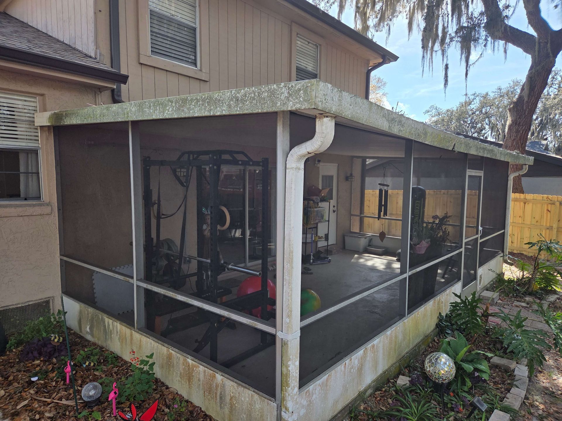 Screened backyard patio with gym equipment beside a house, bordered by plants and a stone path