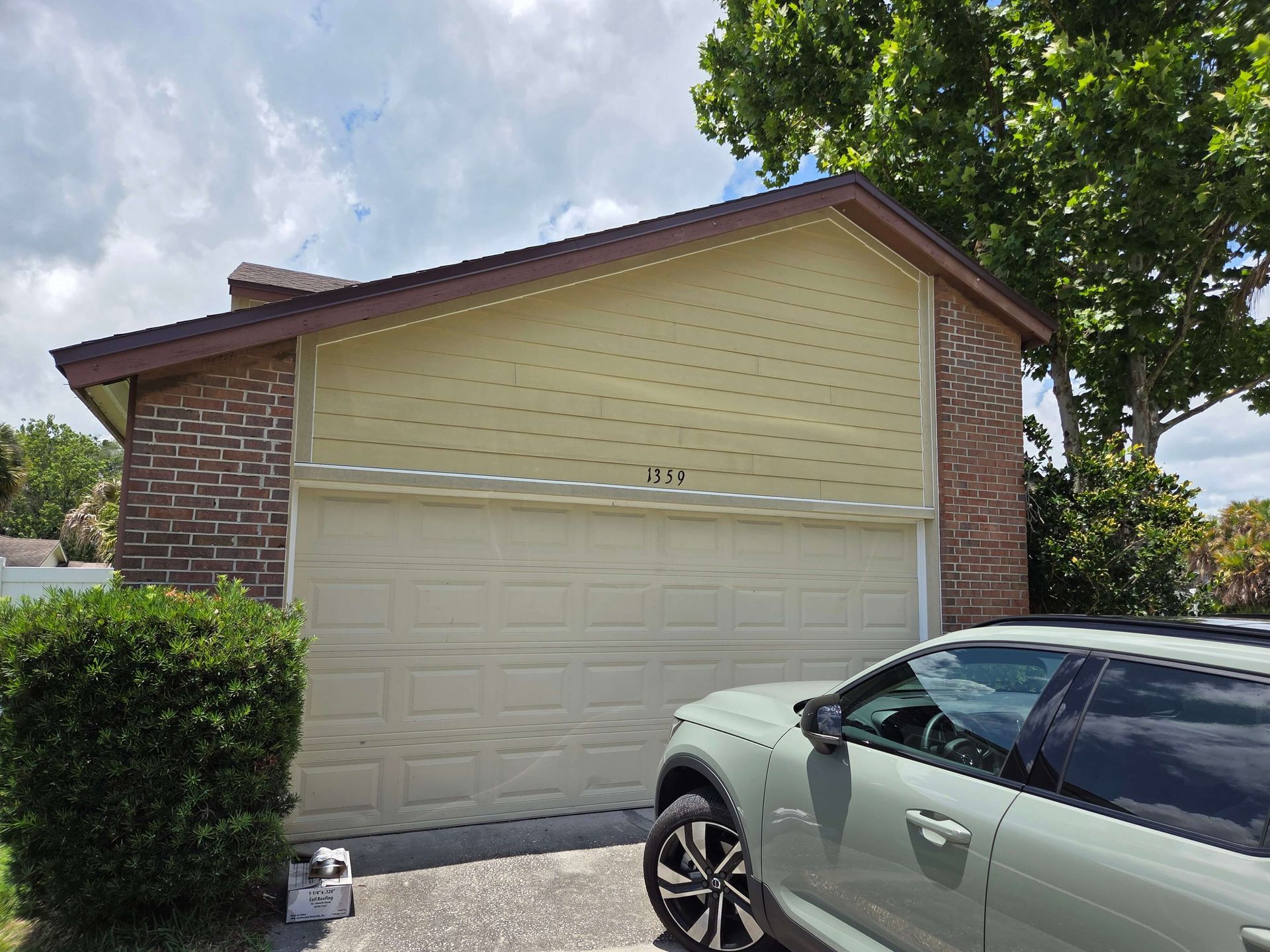 Suburban brick garage with beige siding and a silver car parked in front under a cloudy sky