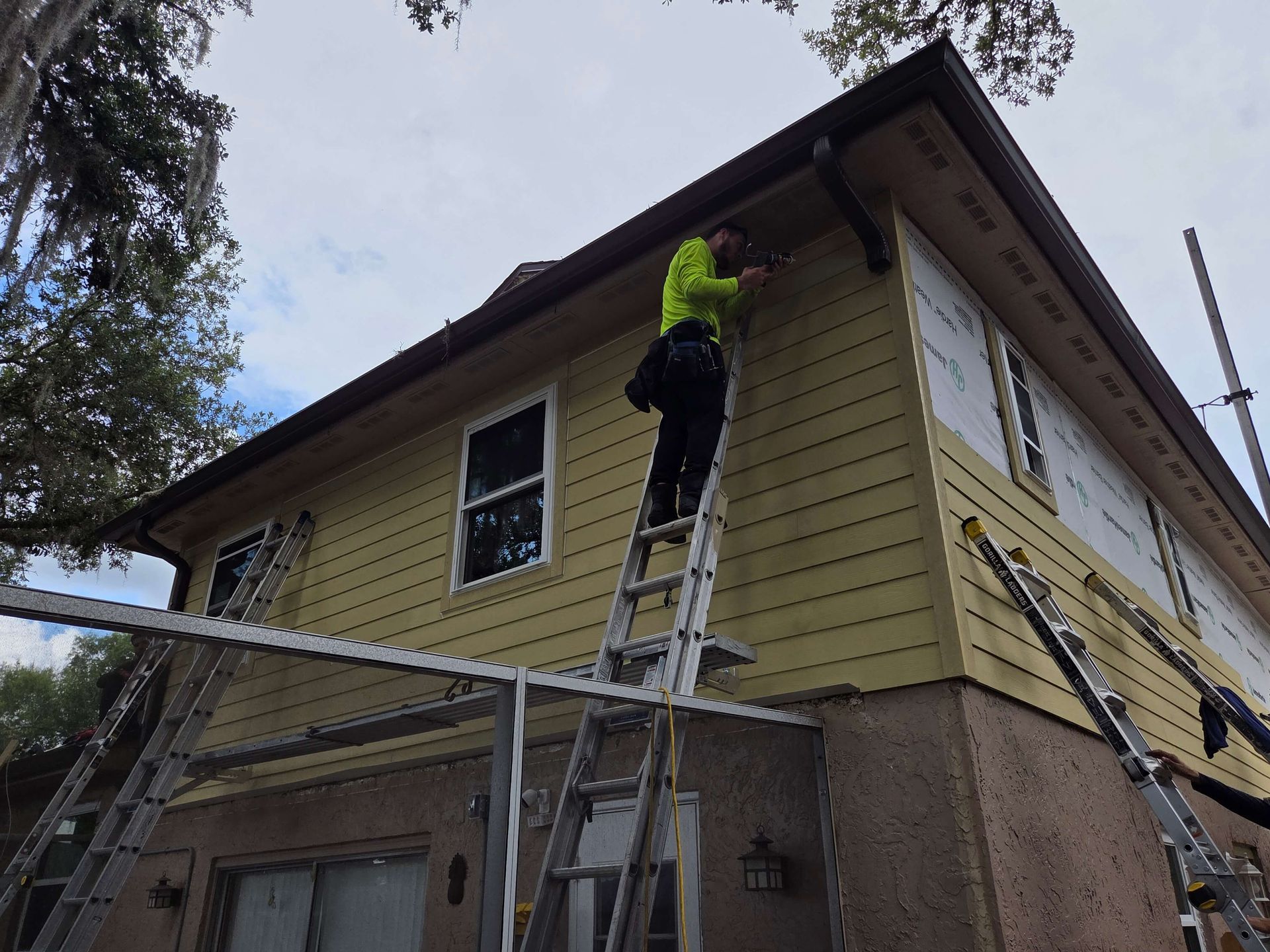 Worker on ladder painting the exterior of a yellow house under construction