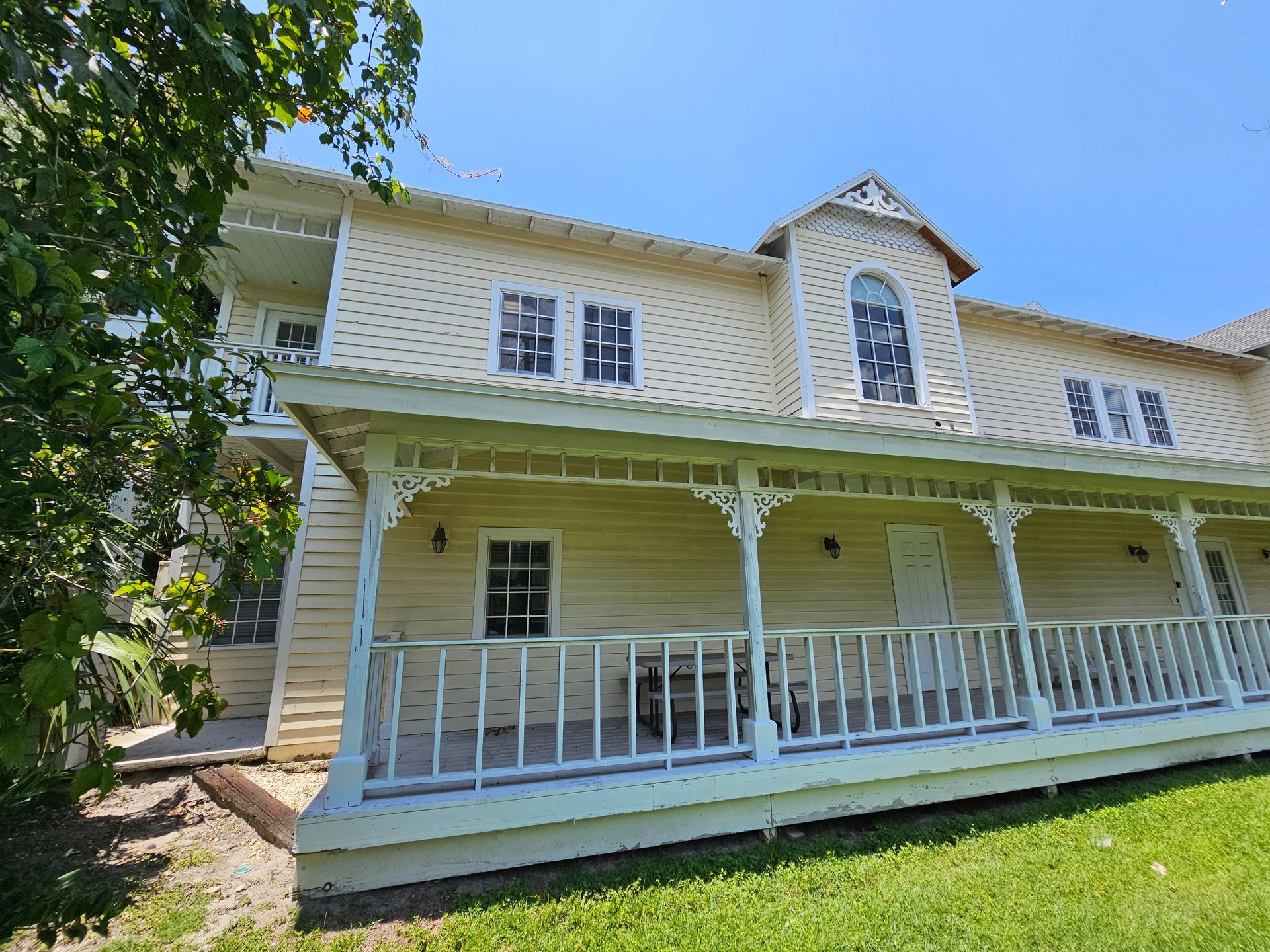 White two-story house with wraparound porch, decorative trim, and green lawn on a sunny day