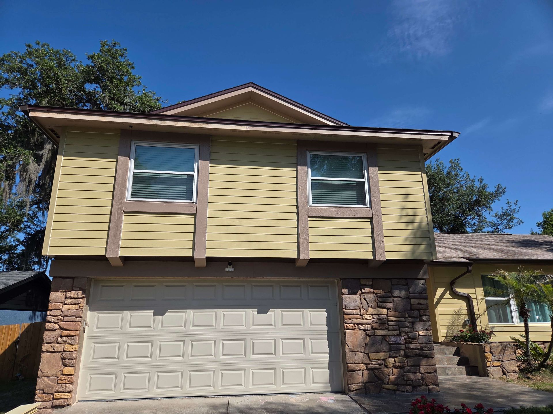 Two-story beige house with a white garage, stone accents, and blue sky above