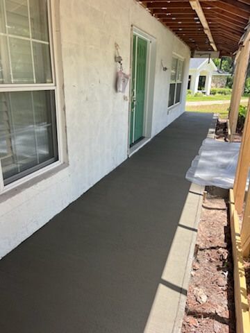 Freshly coated concrete porch beside a white house with green door and windows under a covered roof.