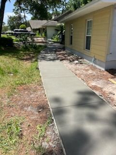 Concrete sidewalk along a yellow house beside a grassy yard on a sunny day
