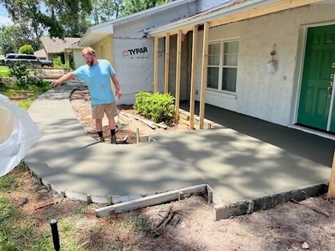 Person standing on a freshly poured concrete ramp beside a building entrance with a green door