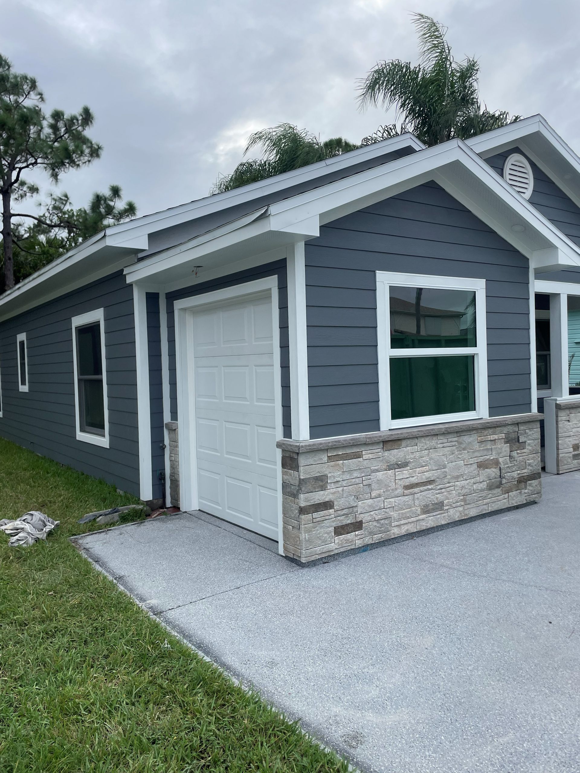 Gray detached garage with white trim, stone base, and a gravel driveway in a grassy yard