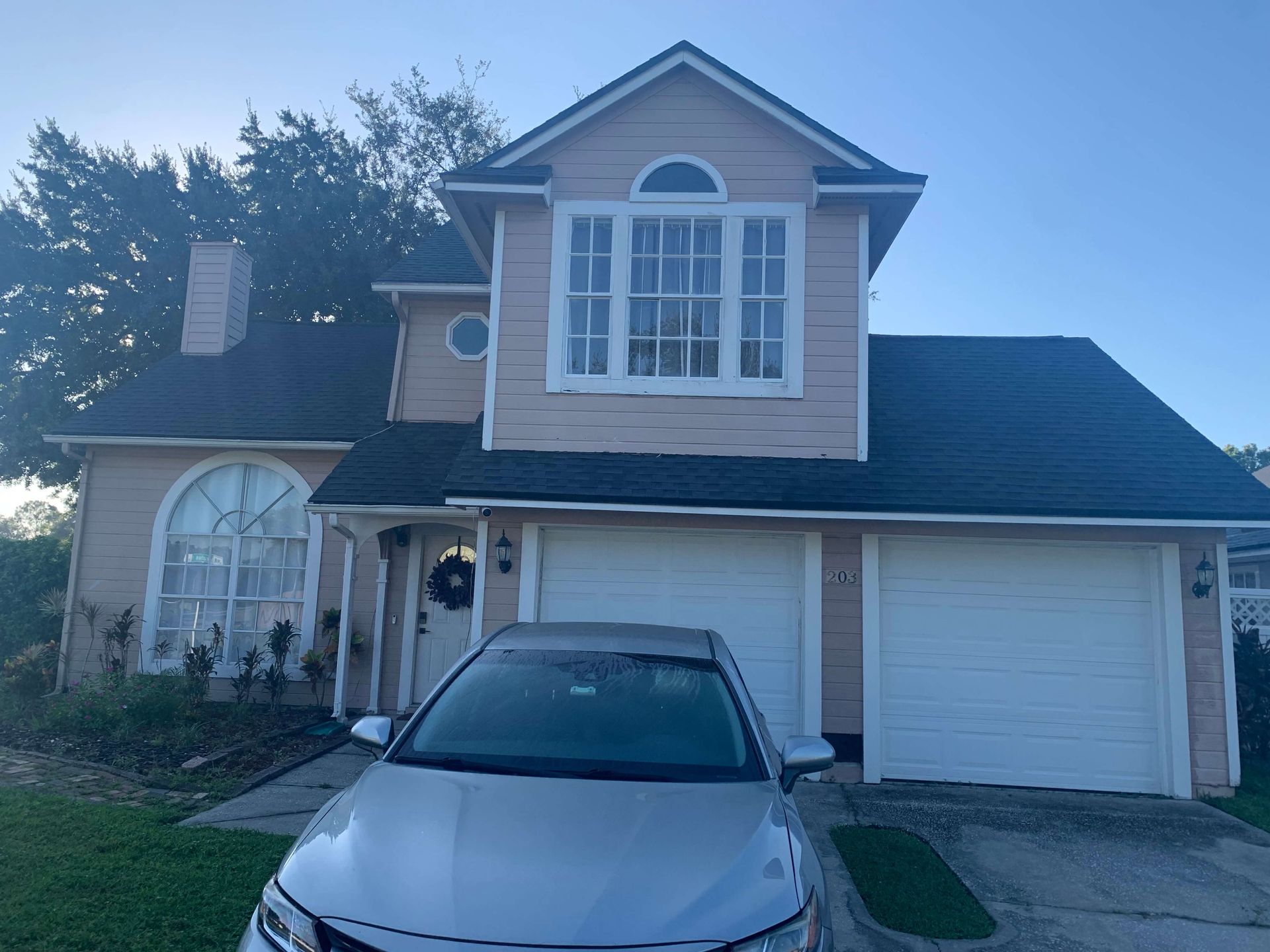 Two-story beige house with a garage and silver car parked in the driveway at dusk