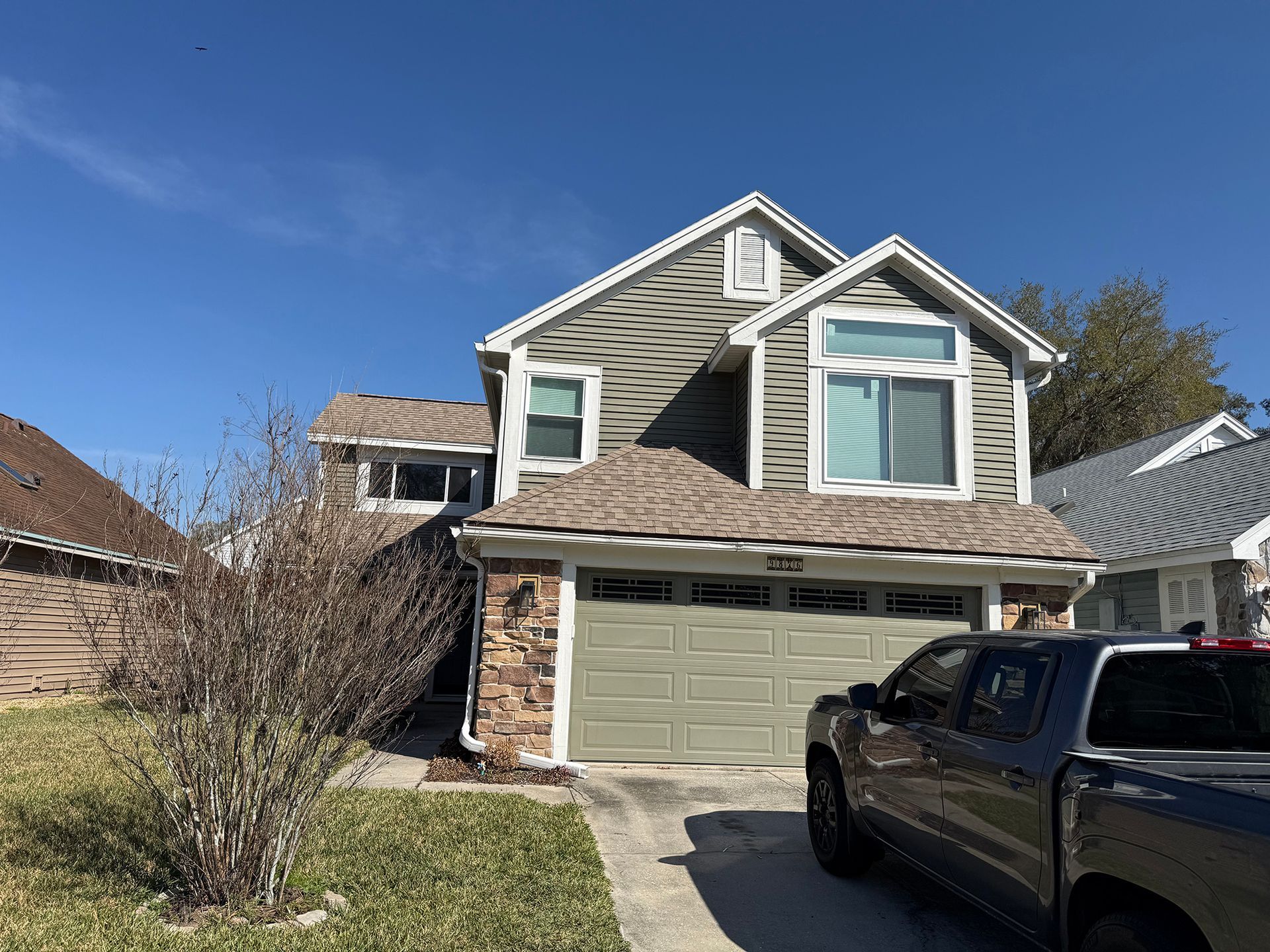 Suburban two-story house with green siding, stone accents, and a black pickup in the driveway
