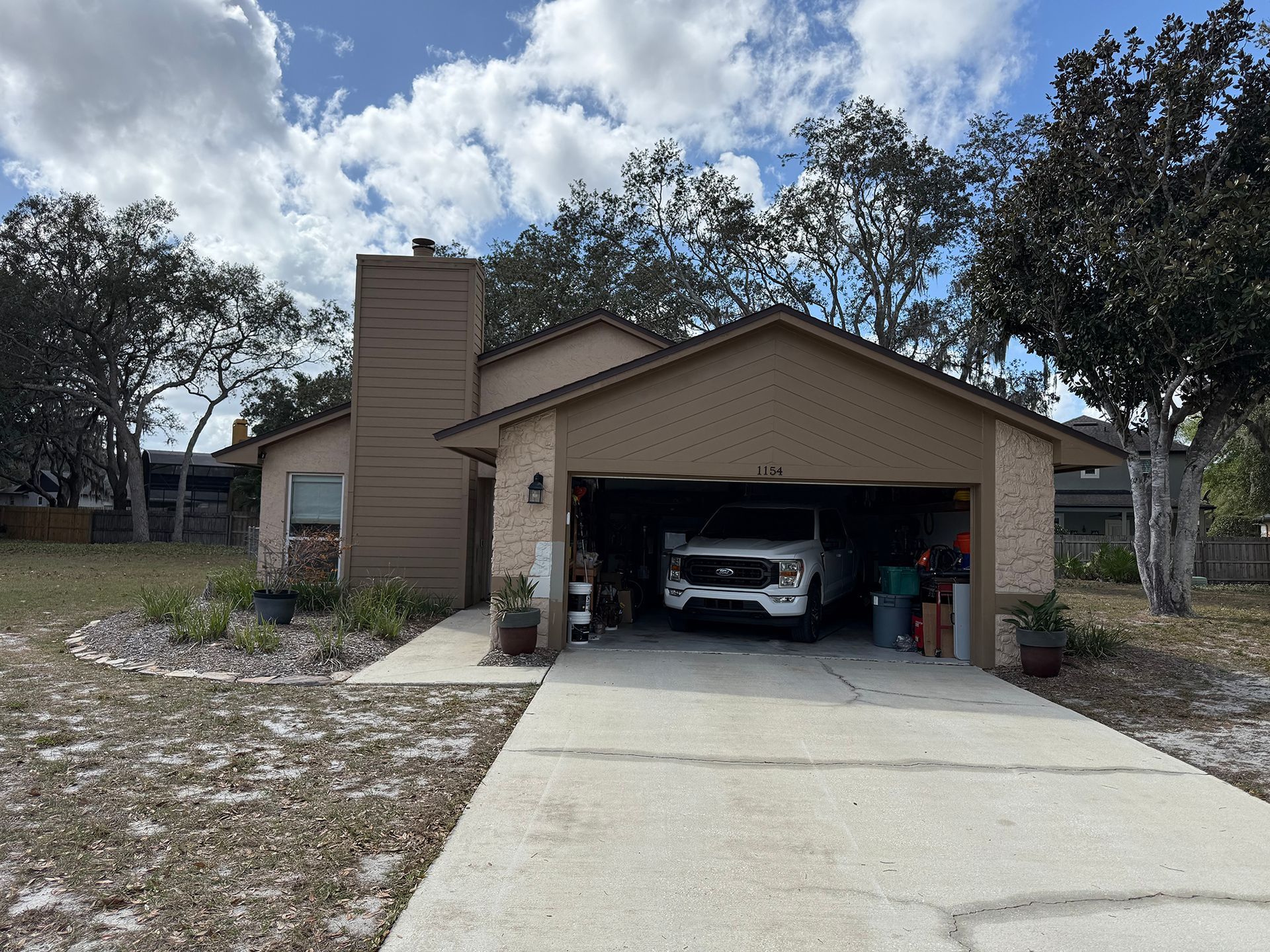 Suburban house with a car in the open garage and a tall brick chimney, viewed from the driveway.