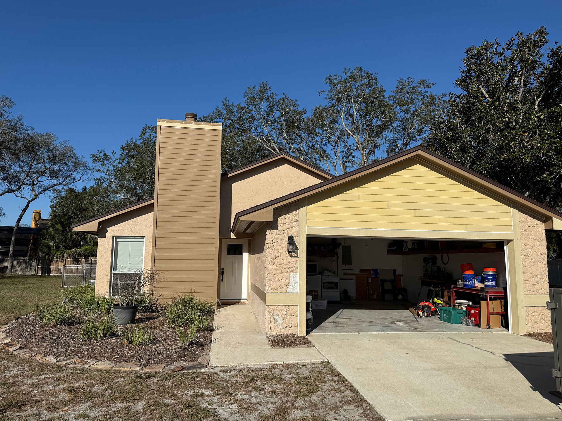 Single-story tan house with open garage, driveway, and clear blue sky