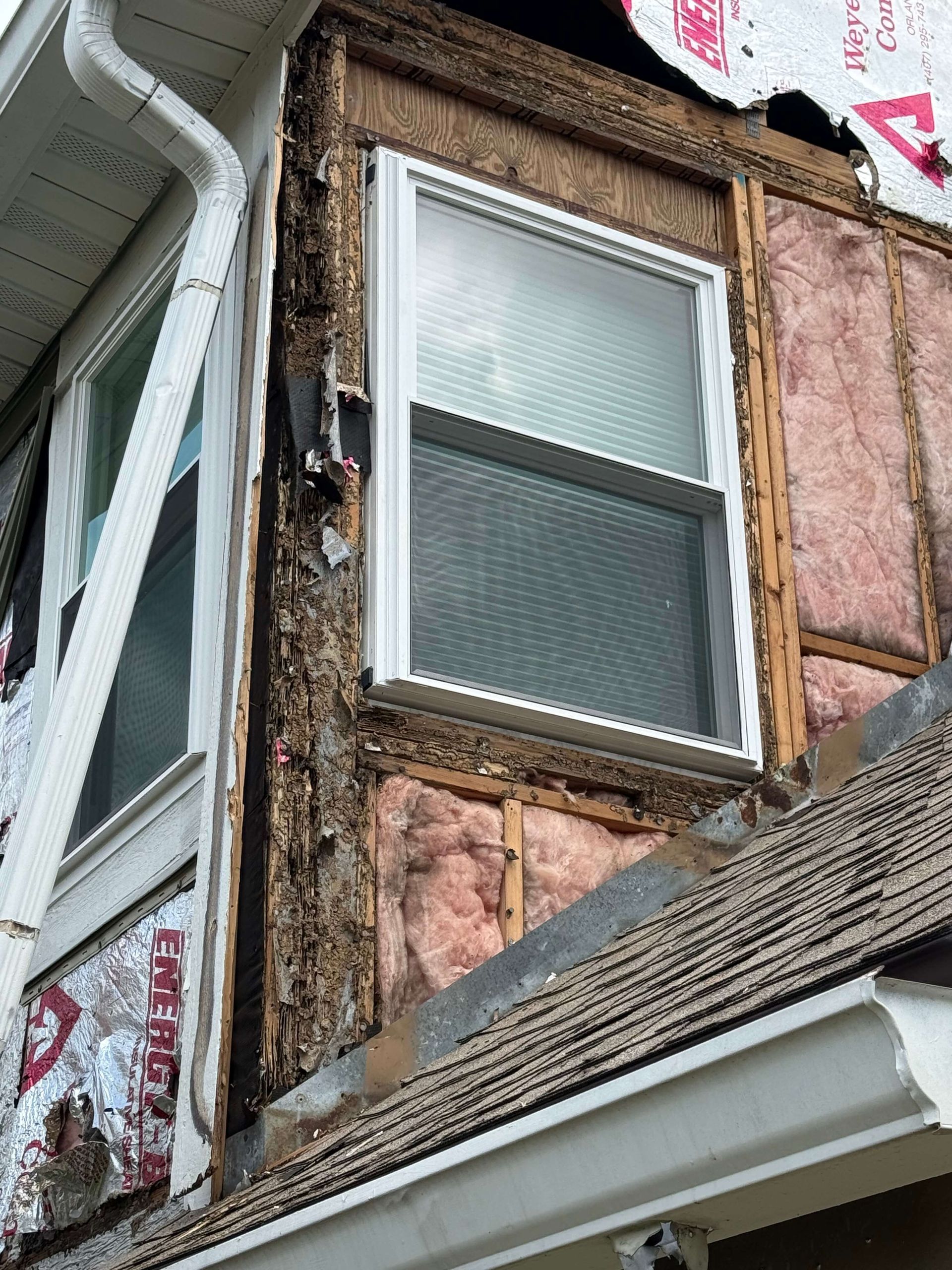 Damaged house exterior with exposed wood, torn siding, and a second-story window above a sloped roof