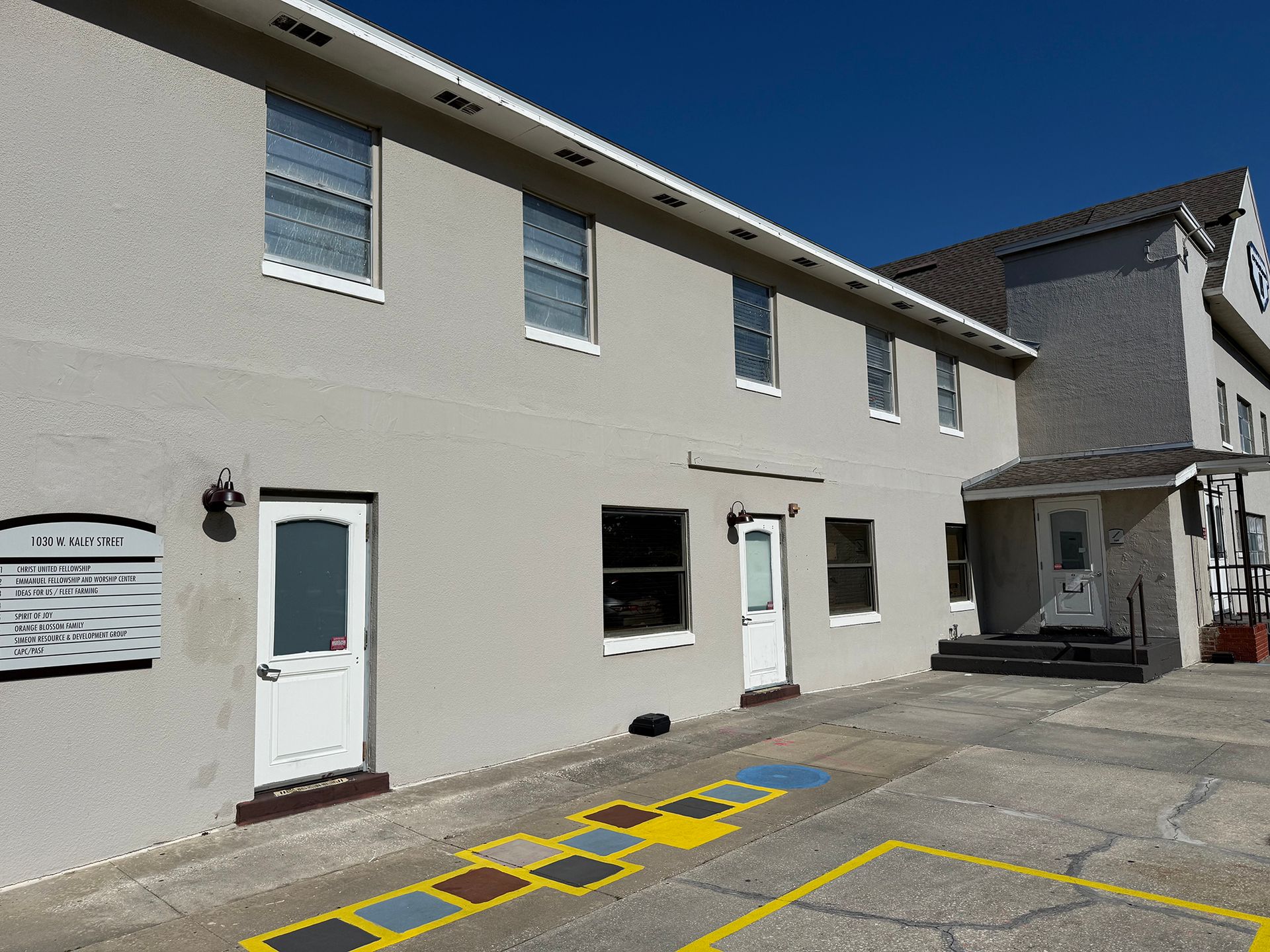 Exterior of a beige building with white doors and windows, and yellow parking markings in front.