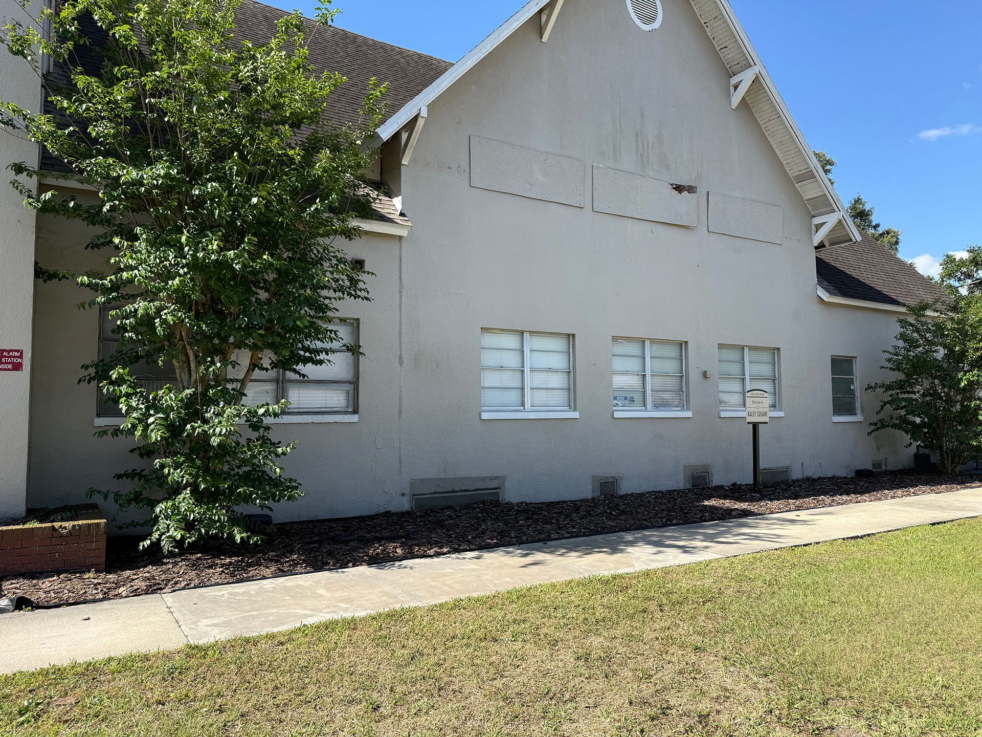 Light gray house exterior with white windows, a tree in front, and a grassy yard under bright sun