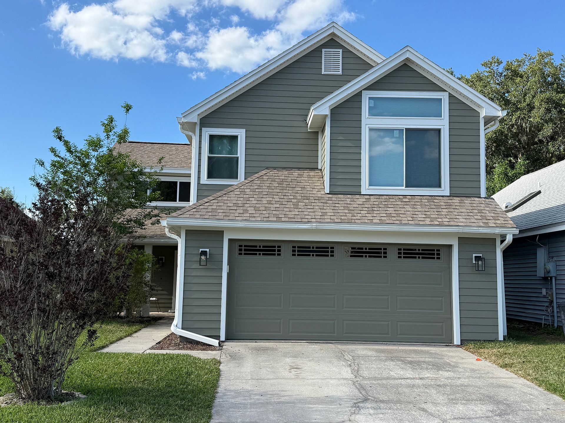 Two-story gray house with a double garage and driveway under a blue sky