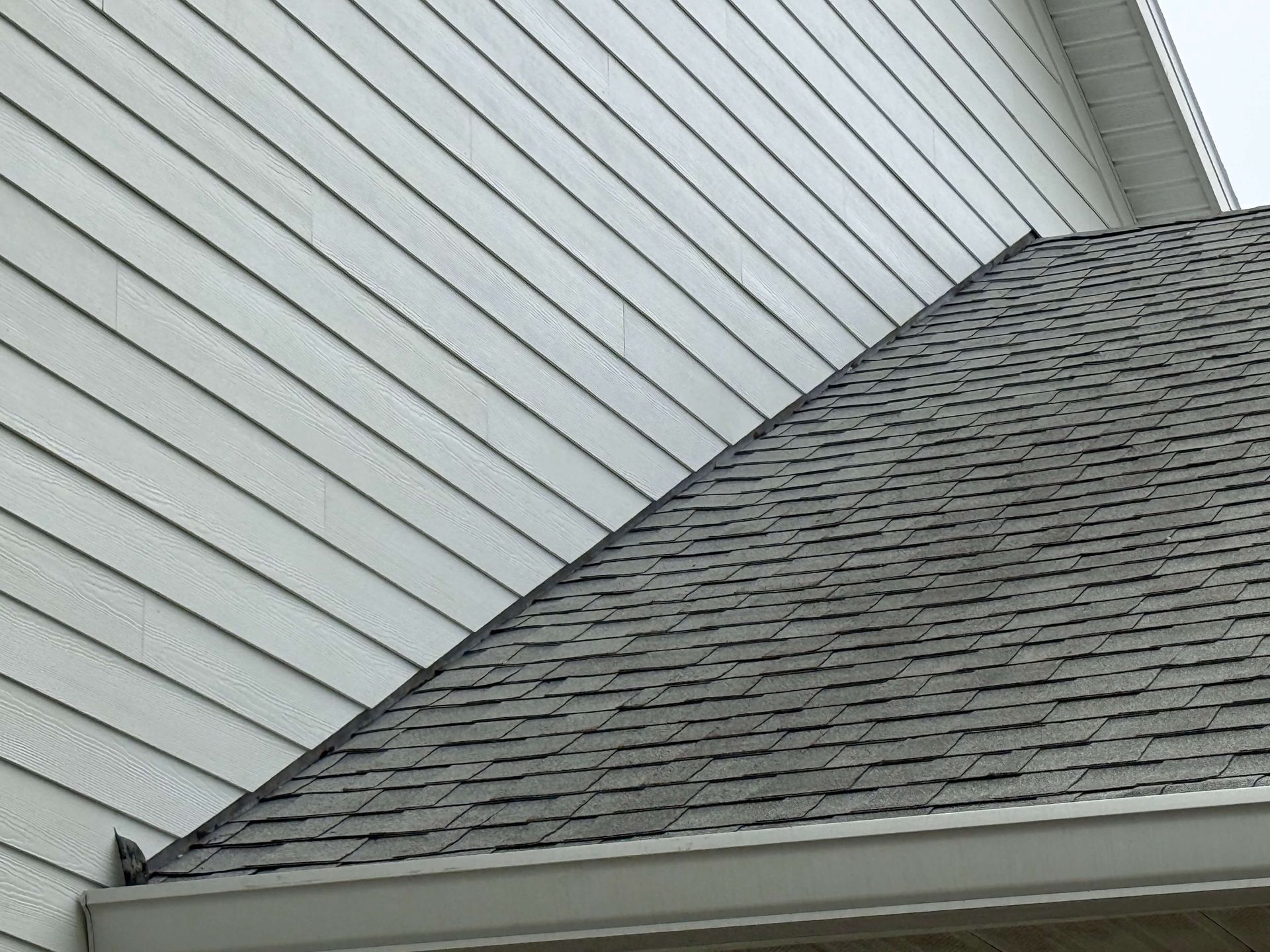 Close-up of a house roof with gray shingles and white siding on the side wall