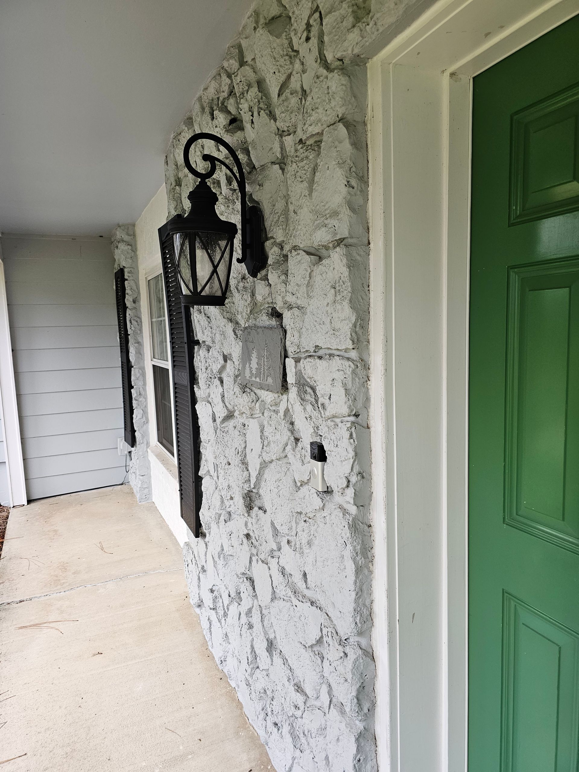 Porch wall with black lantern and green door beside a white-painted hallway
